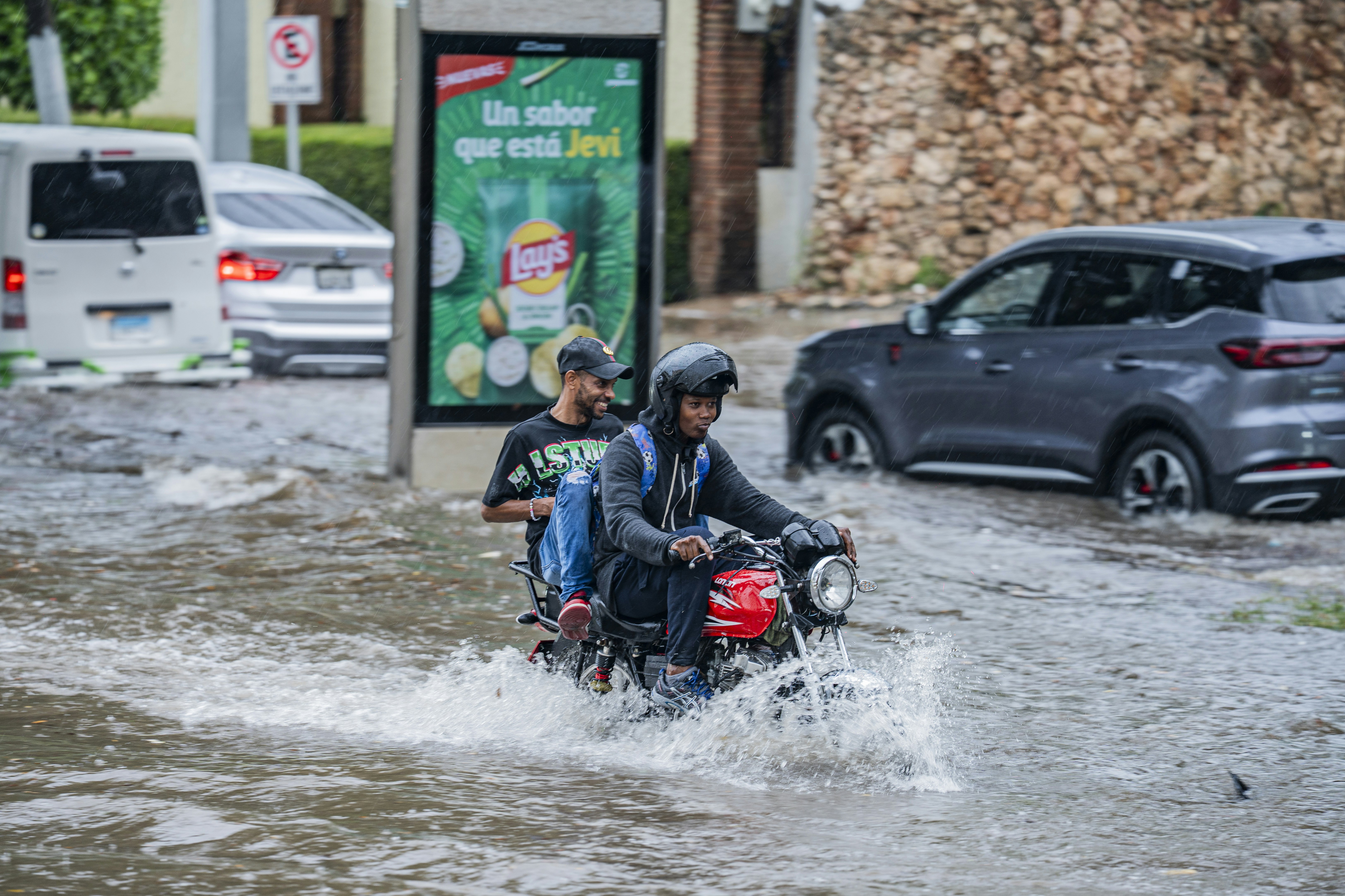 Two people riding a red motorcycle through a flooded city street during rain