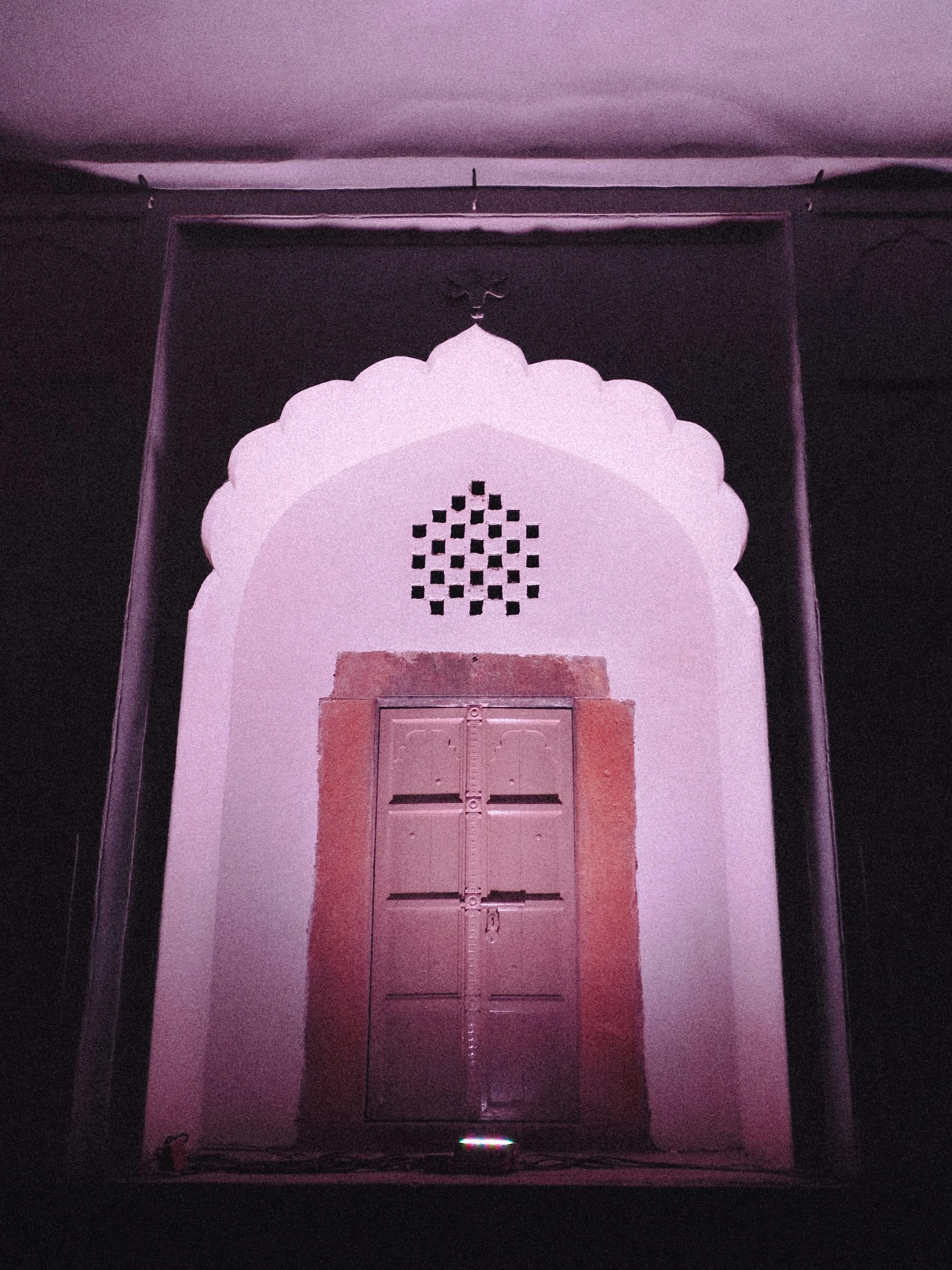 An arched doorway with a lattice window under purple light in a dark wall