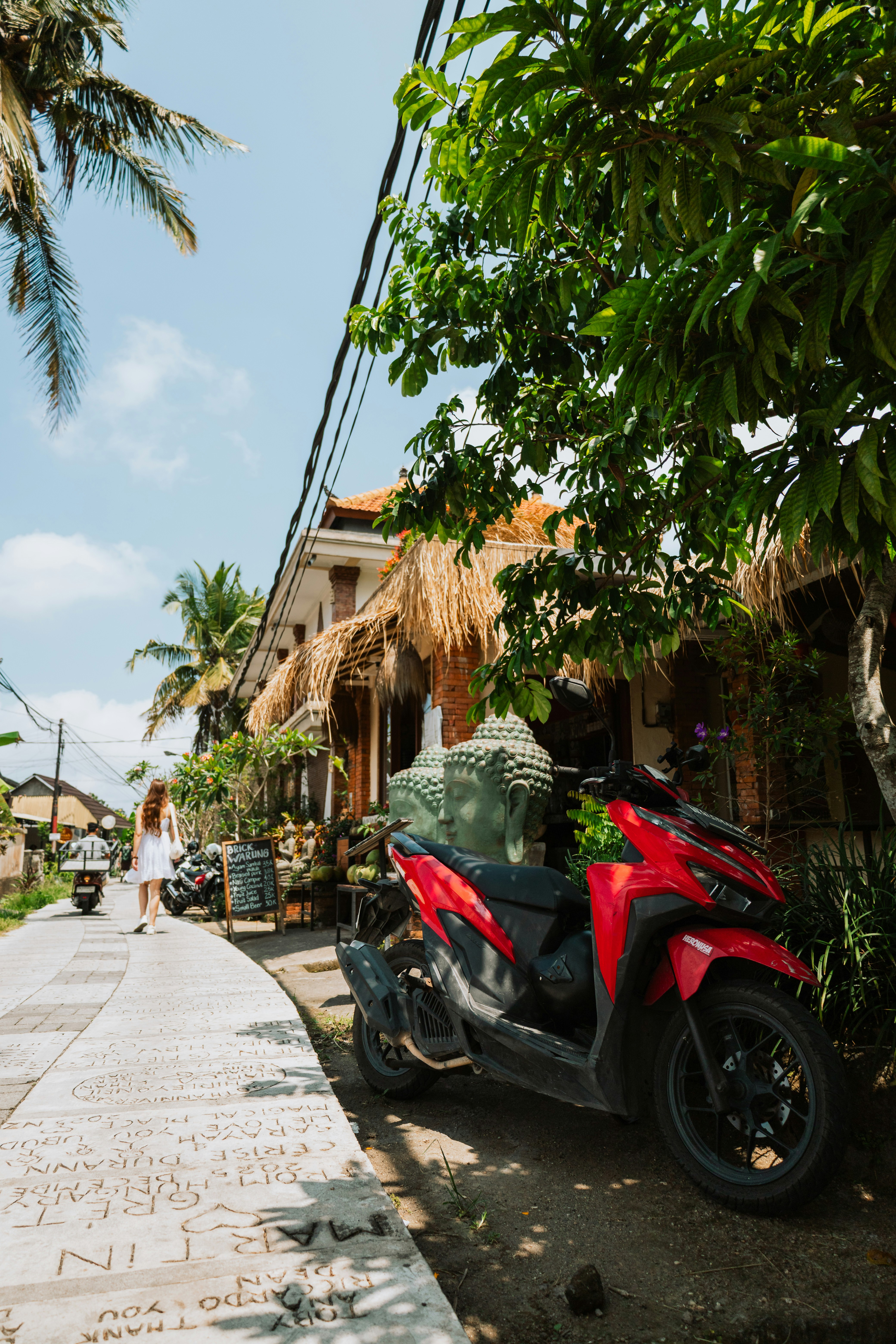 A red scooter parked on a path beside a building with Buddha statues
