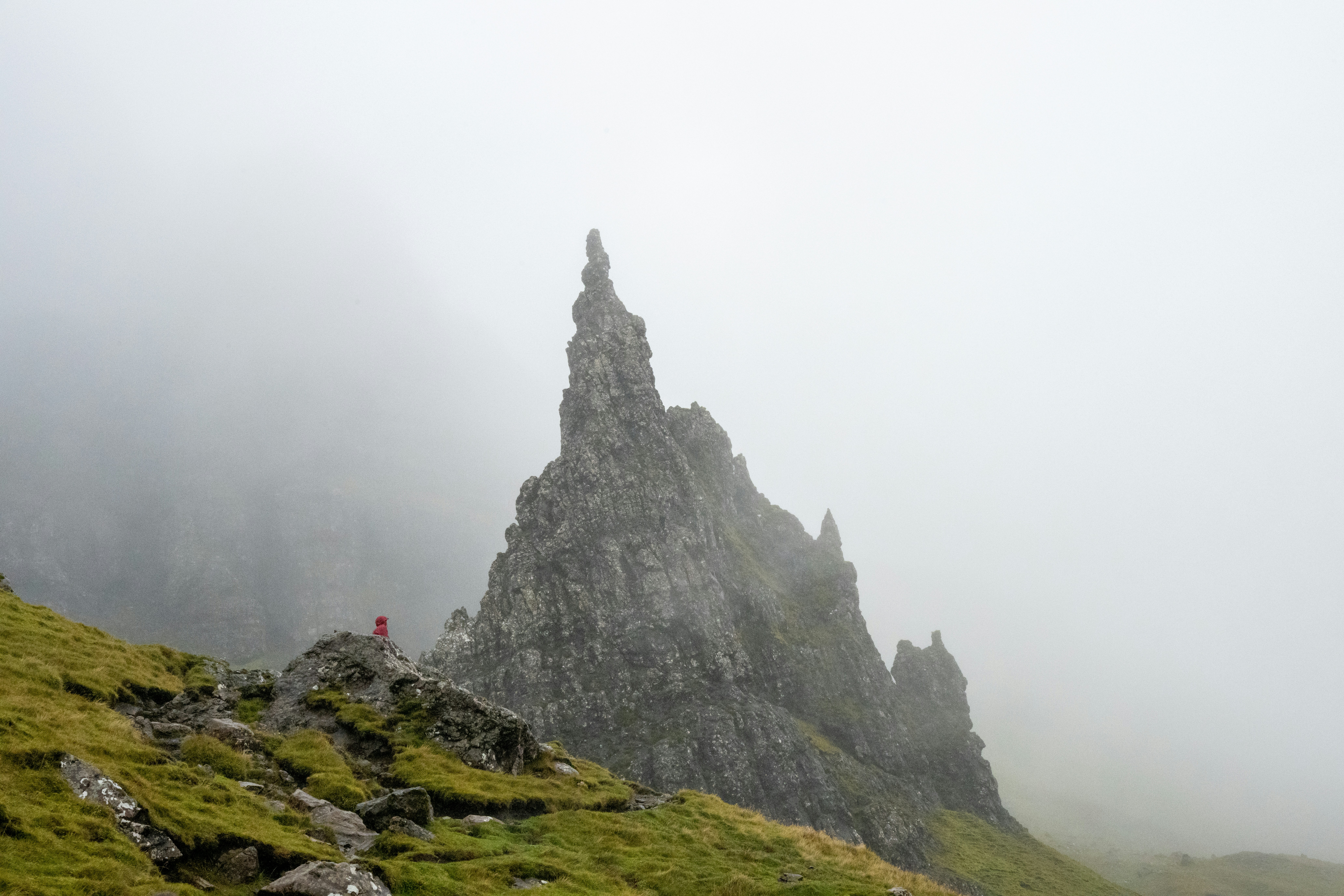 A person in a red jacket on a rocky outcrop in thick fog