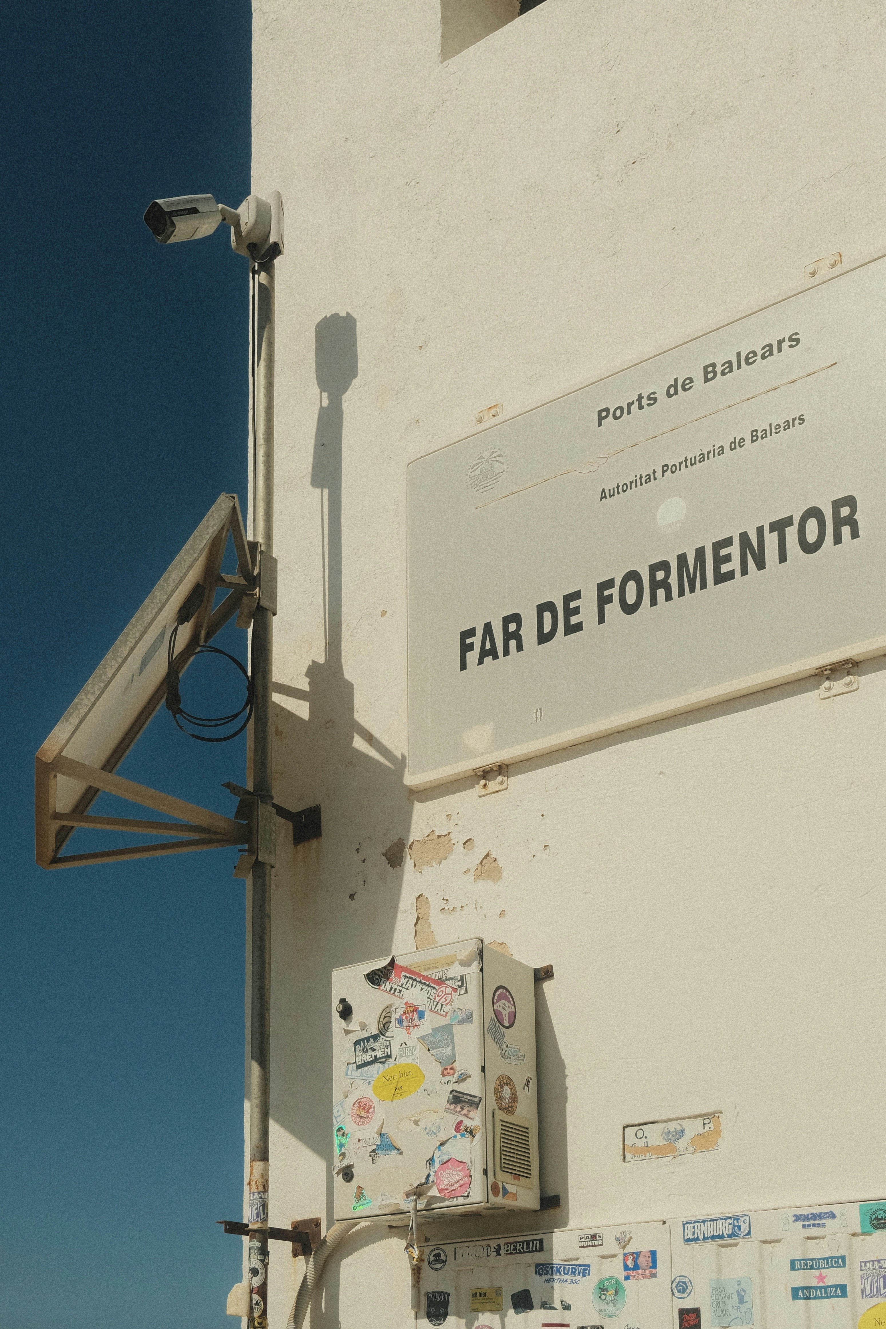 Fotomural A sign reading Far de Formentor on a white wall with stickers