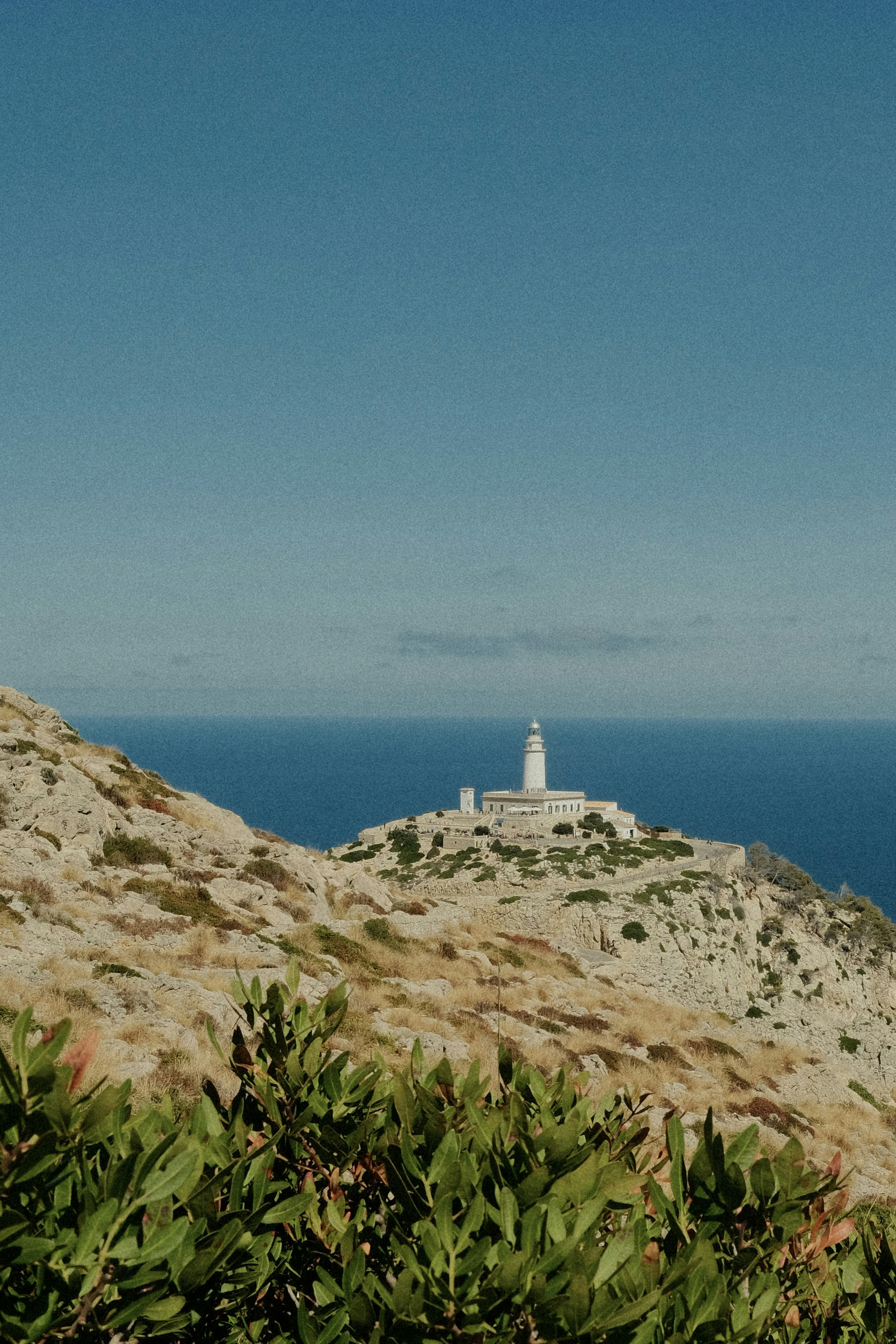 A white lighthouse on a rocky cliff overlooking the deep blue sea