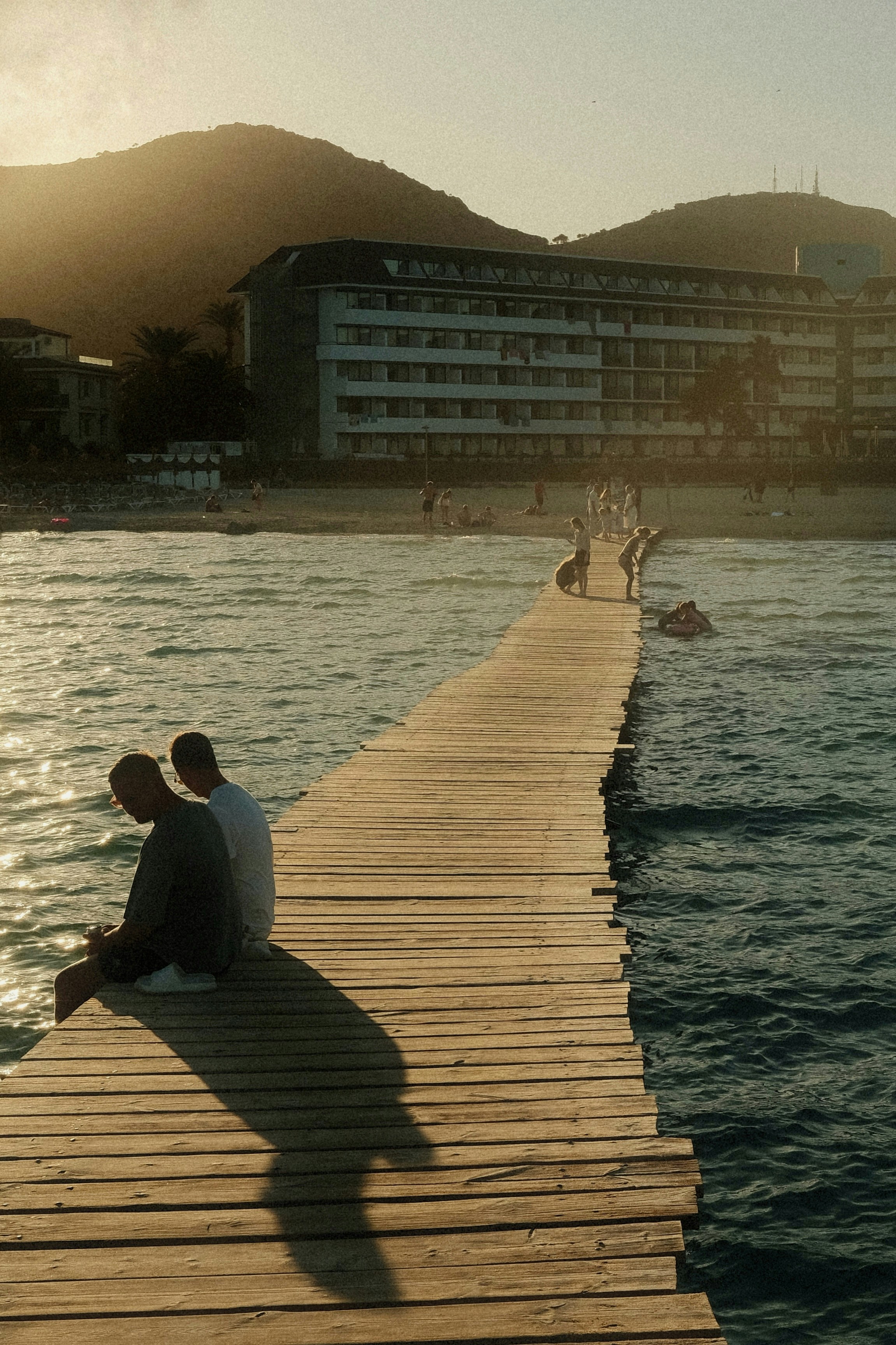 Two people on a wooden pier extending into the sea at golden hour