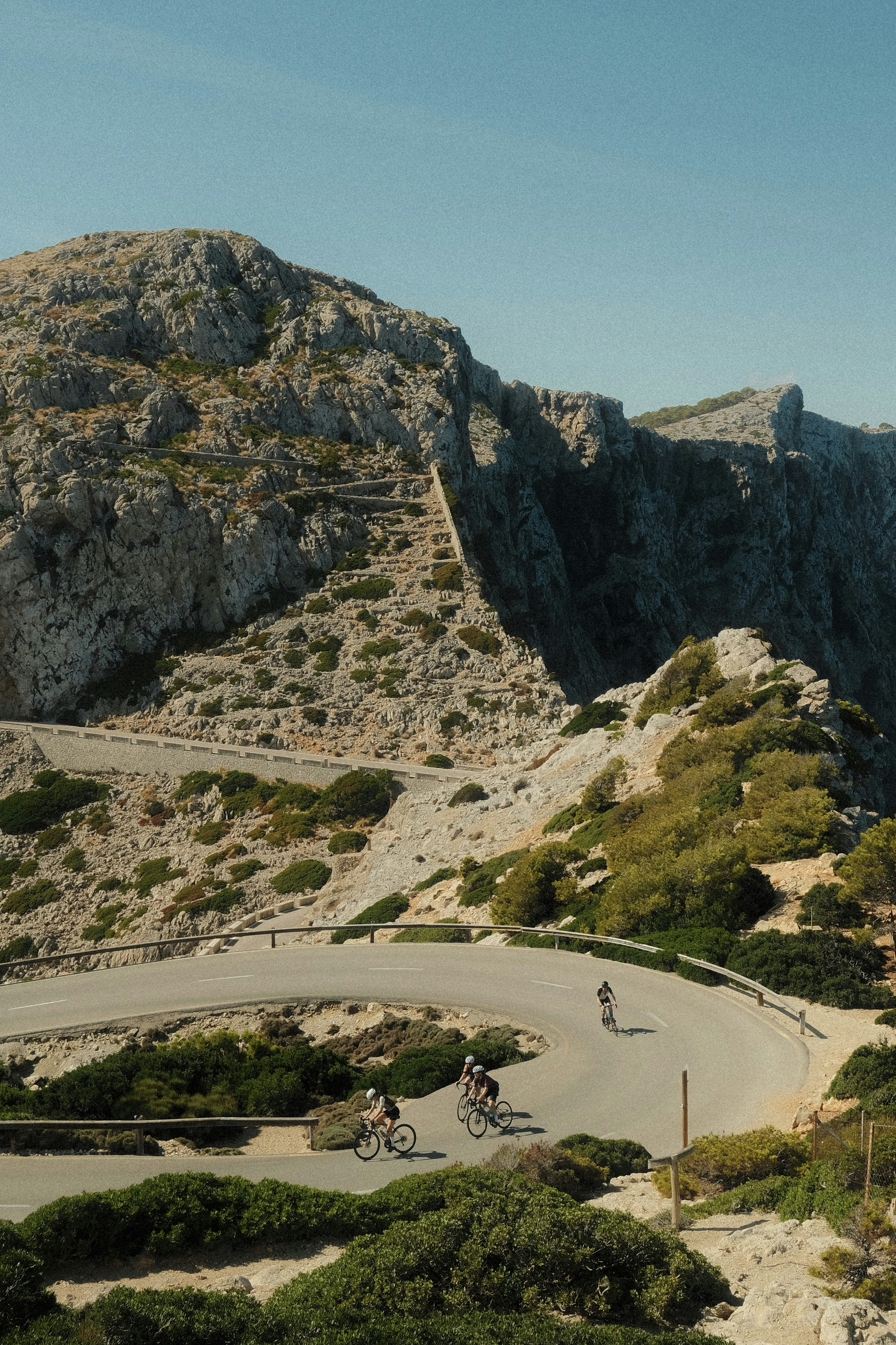 Three cyclists riding on a winding mountain road in Mallorca, Spain