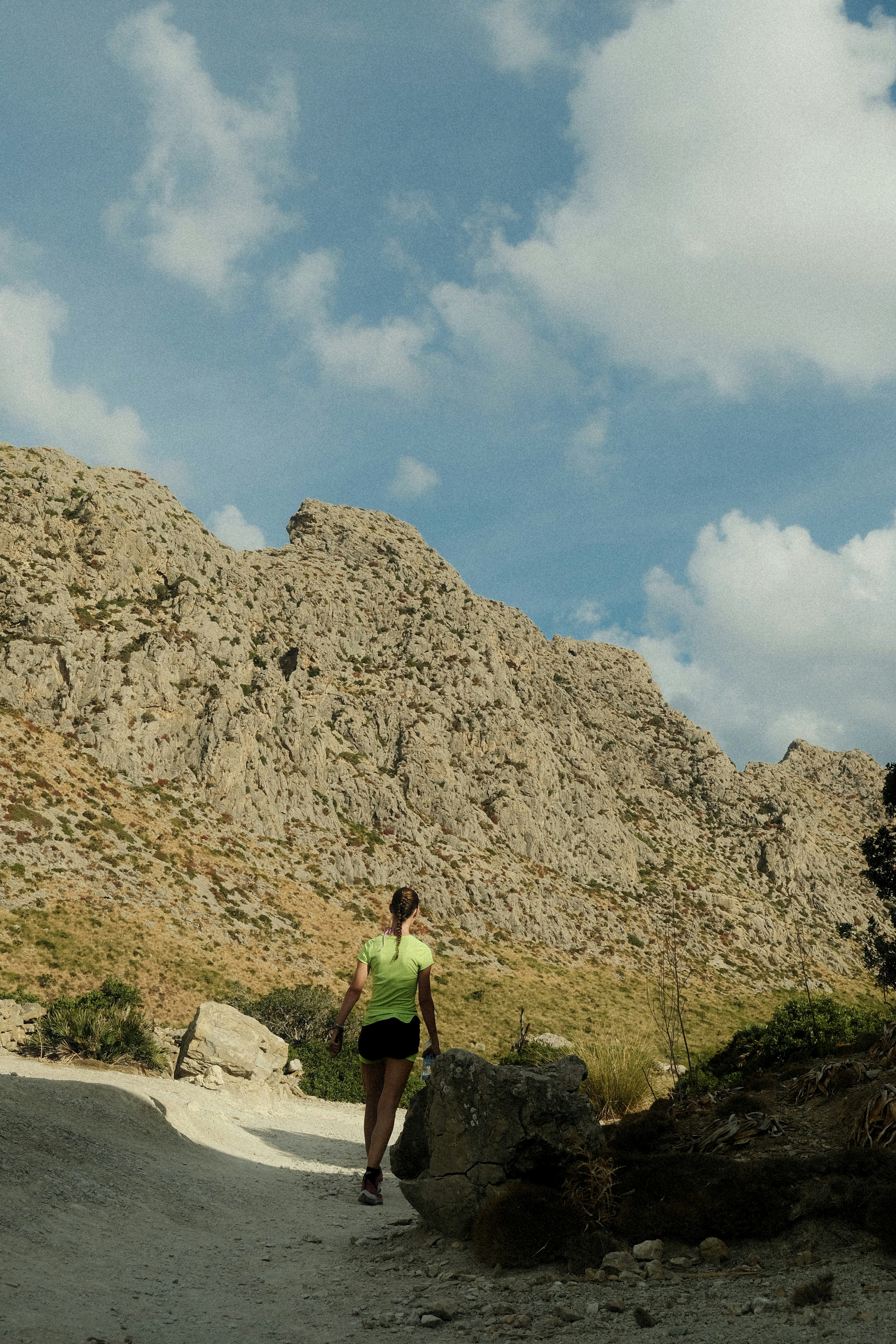 A person in a neon green shirt walking on a rocky trail toward mountains