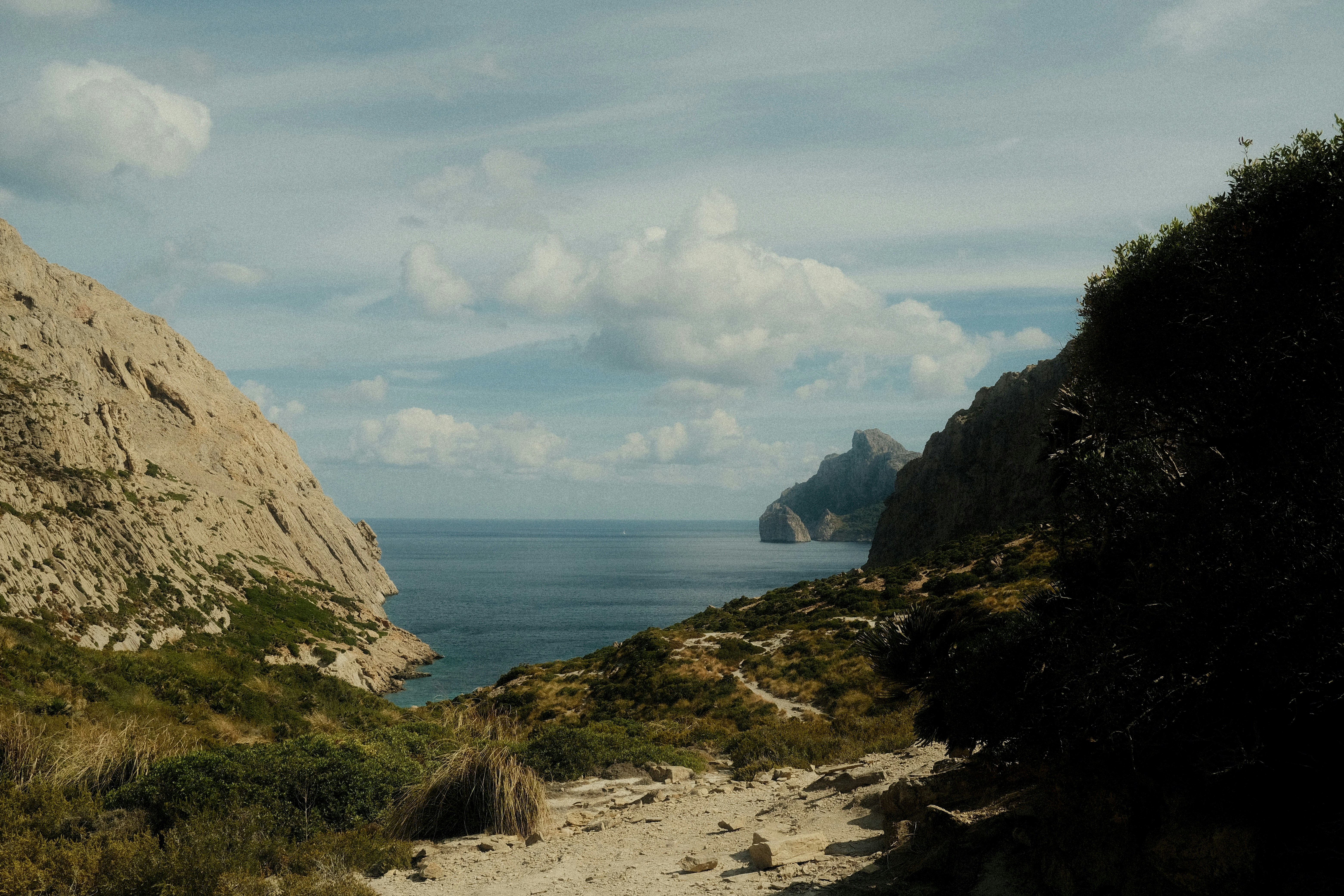 A dirt path leading toward a rocky coastal inlet with blue water