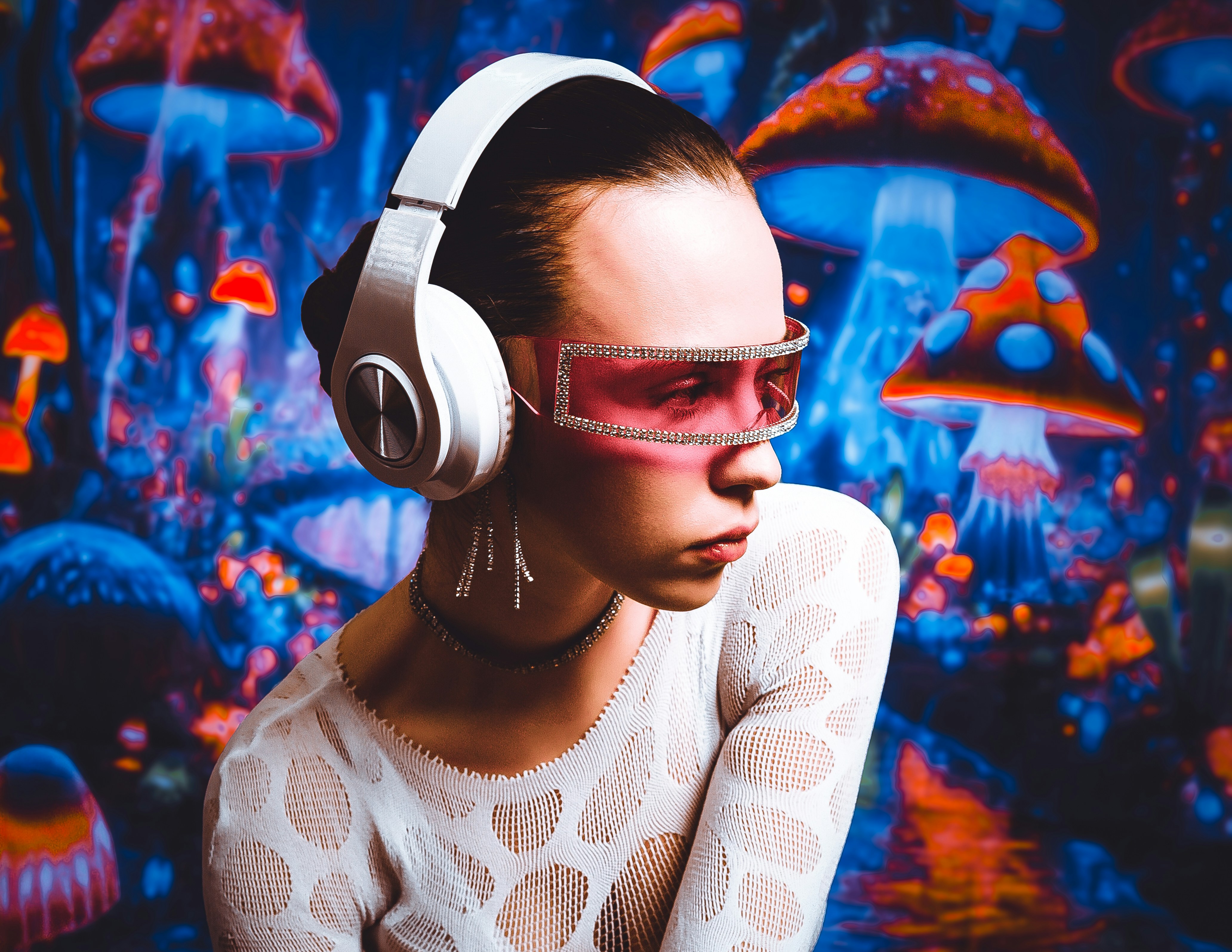 A person wearing white headphones and pink visor glasses against a glowing mushroom background