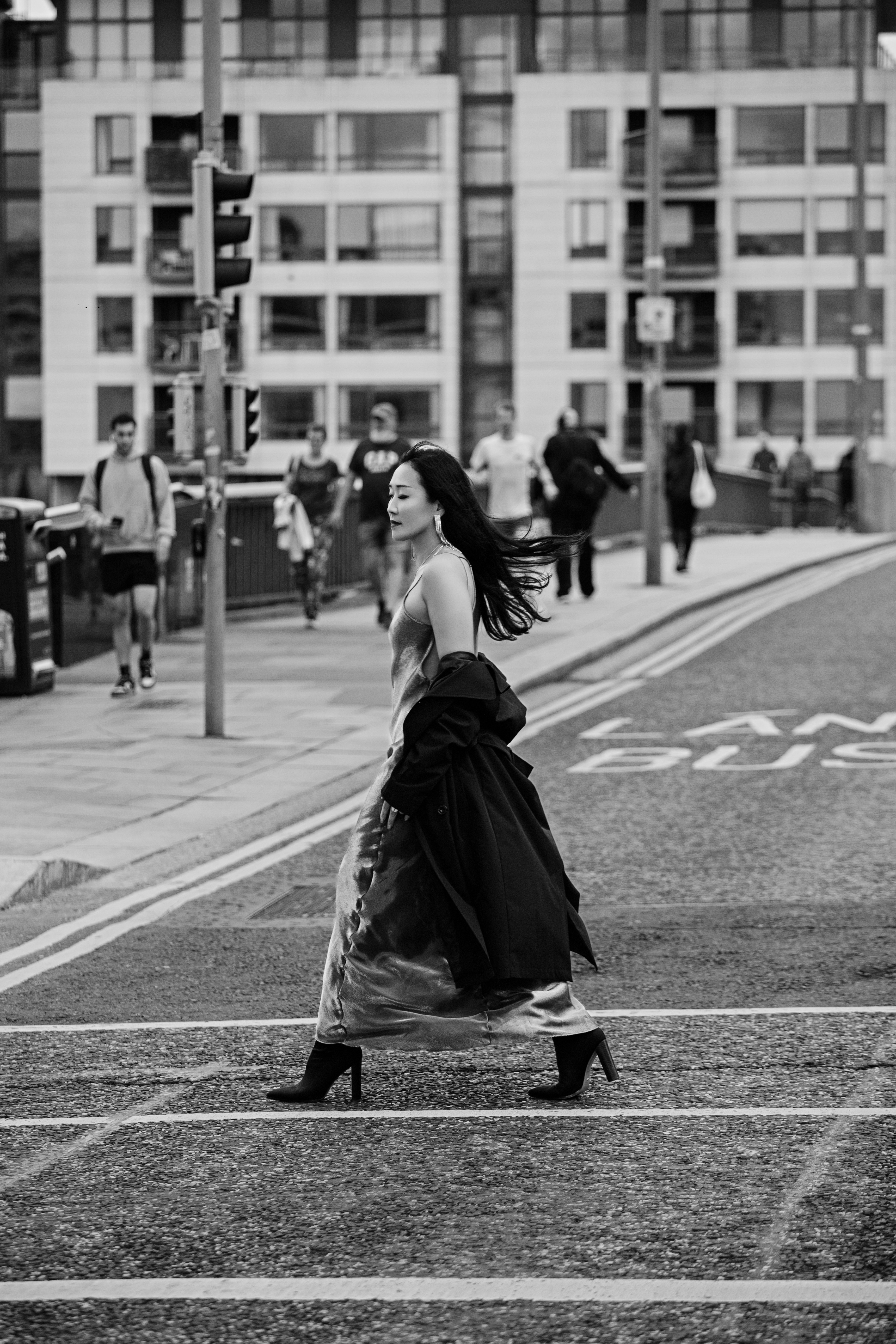 A woman in a long dress and coat walking across a city street