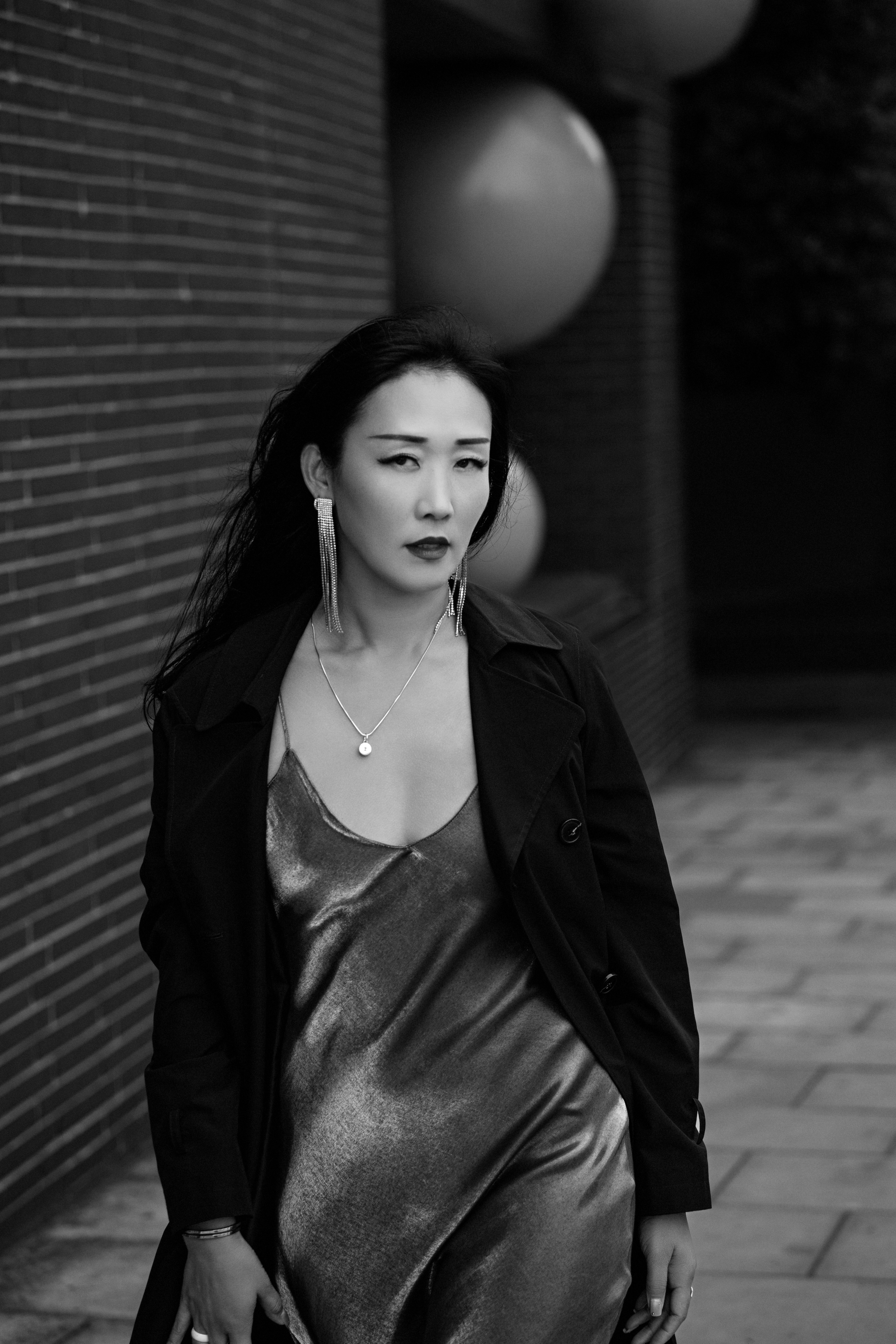 A woman in a satin slip dress and trench coat with long dangling earrings
