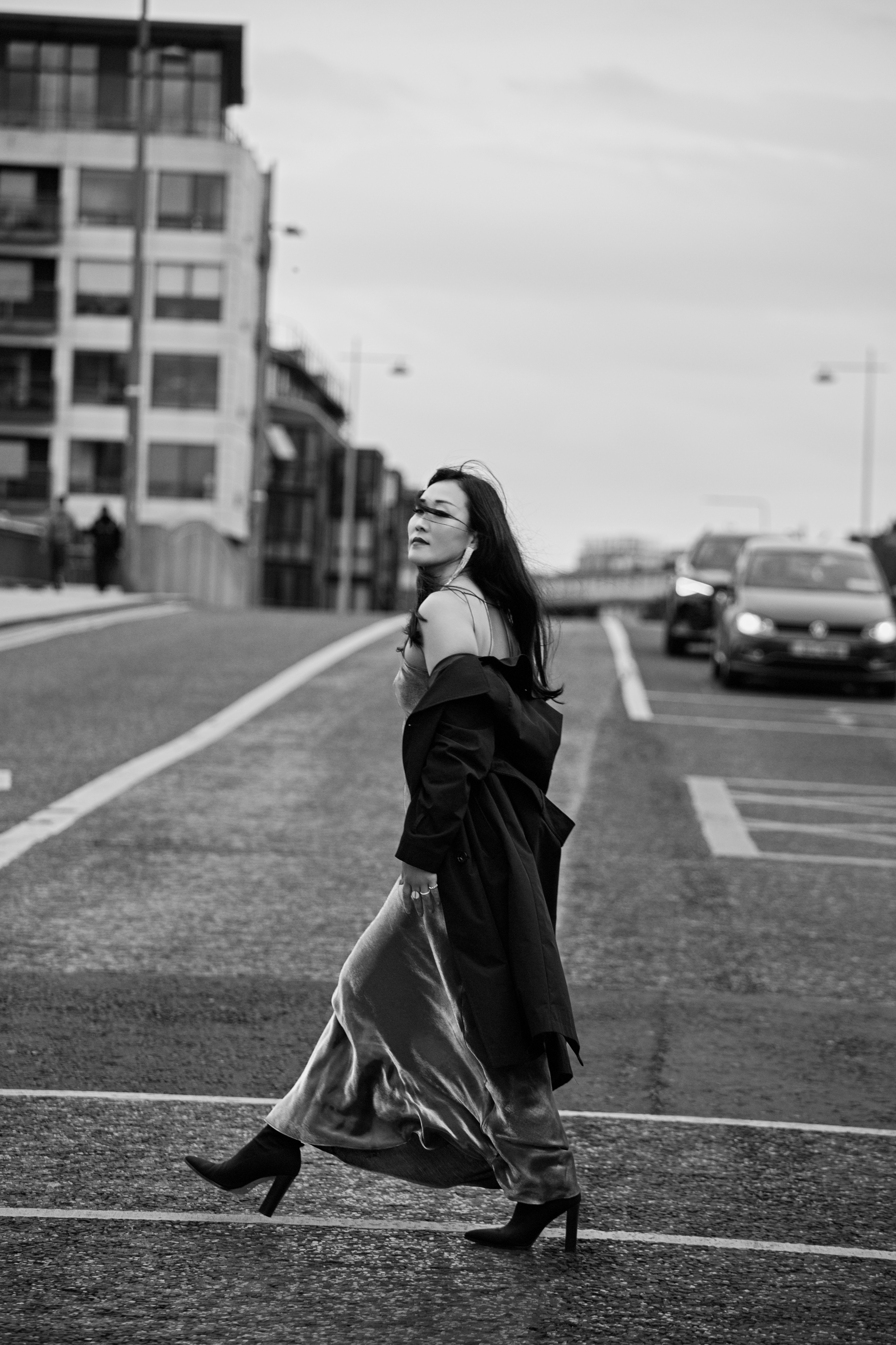 A woman in a long dress and coat walking across a city street