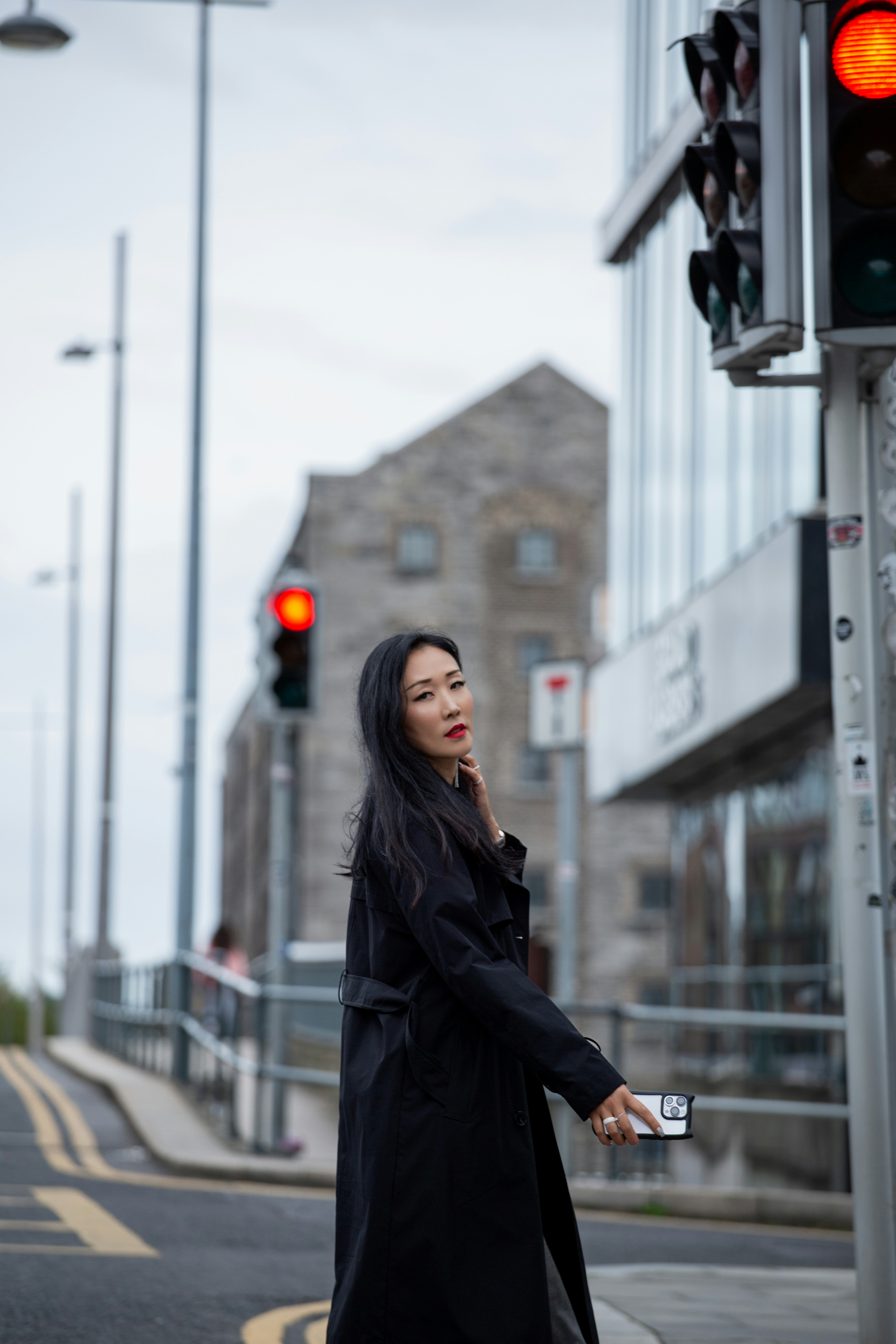 A woman in a black trench coat holding a smartphone on a city street