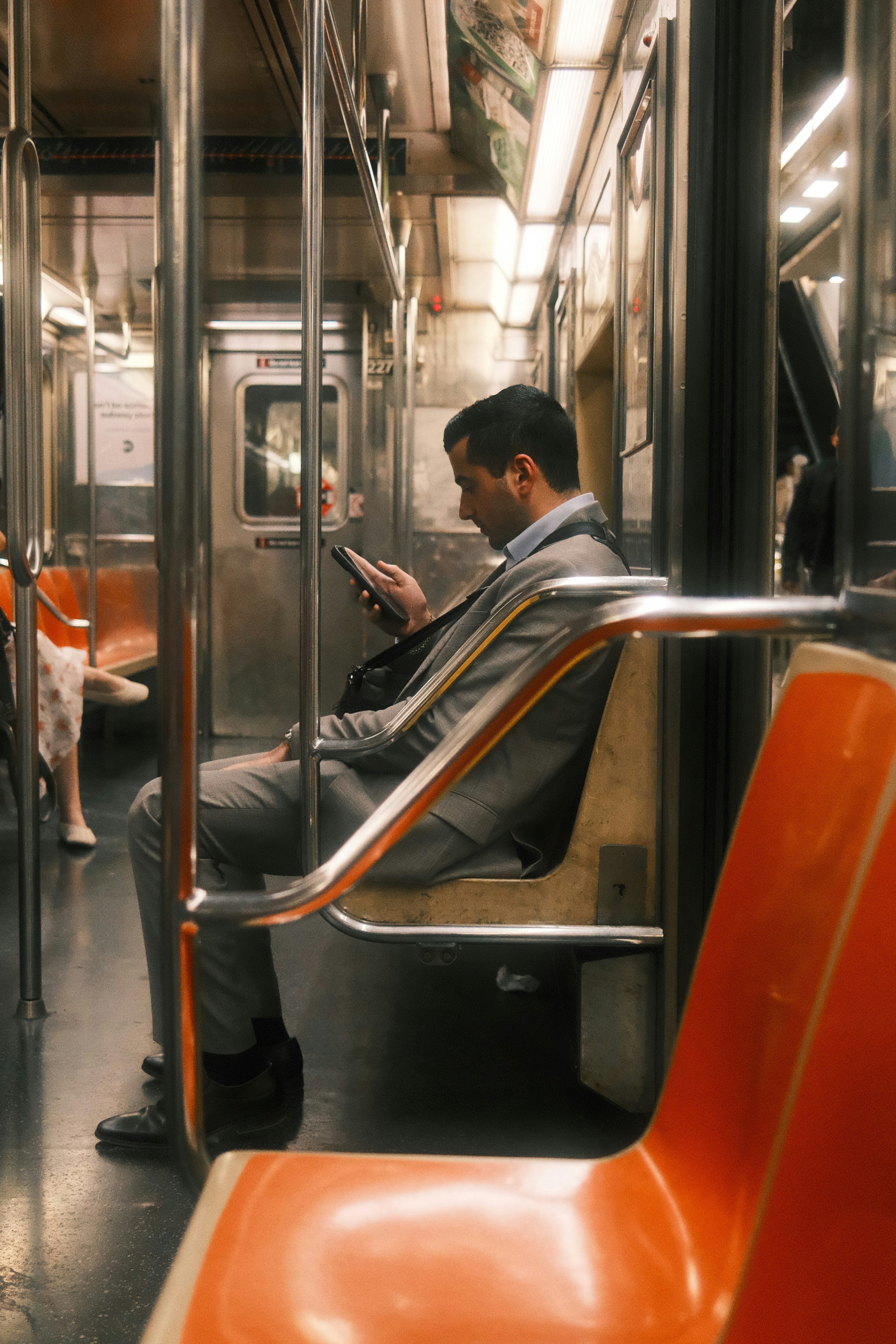 A man in a grey suit using a smartphone on a subway train