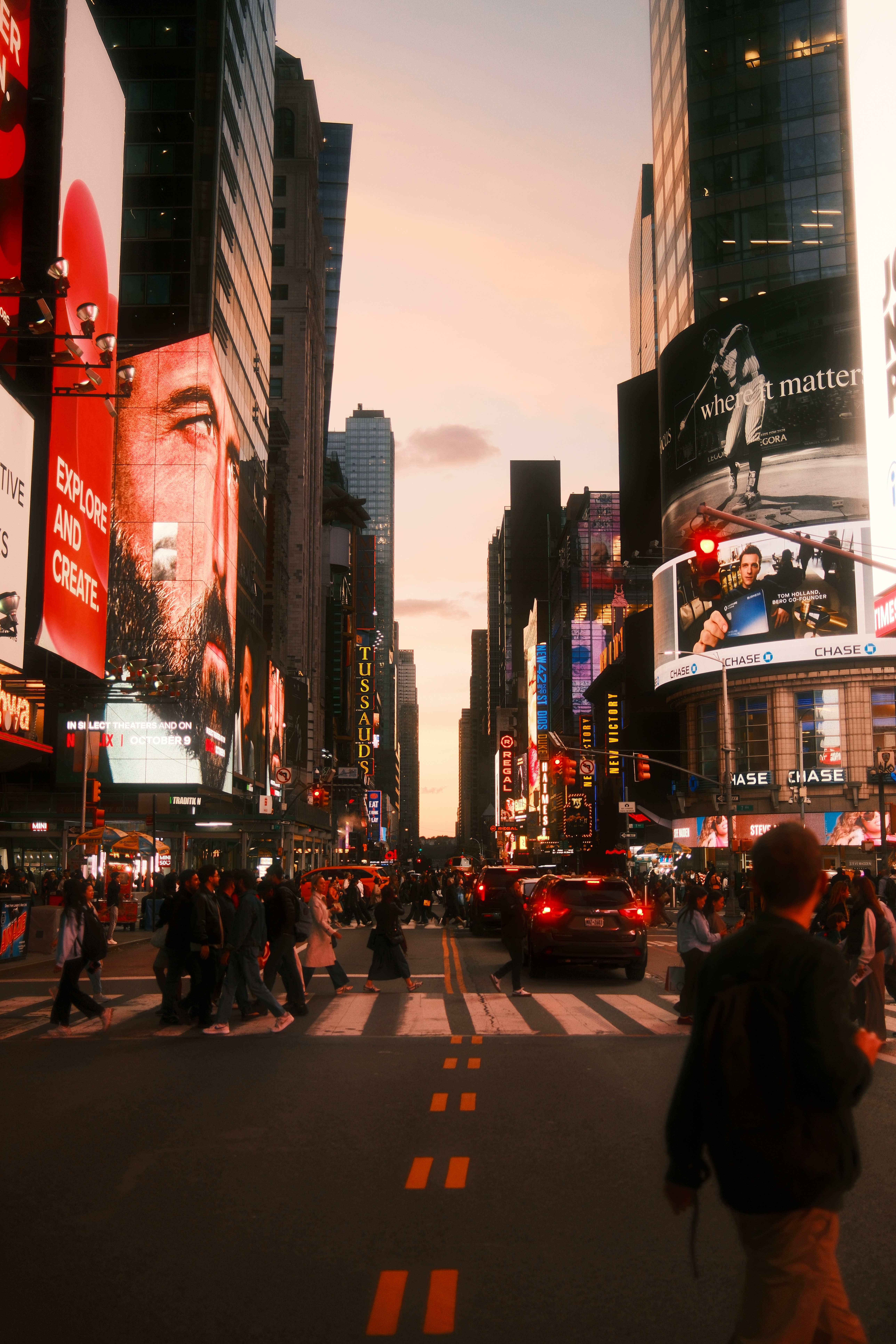 People crossing a busy street in Times Square under large illuminated digital billboards
