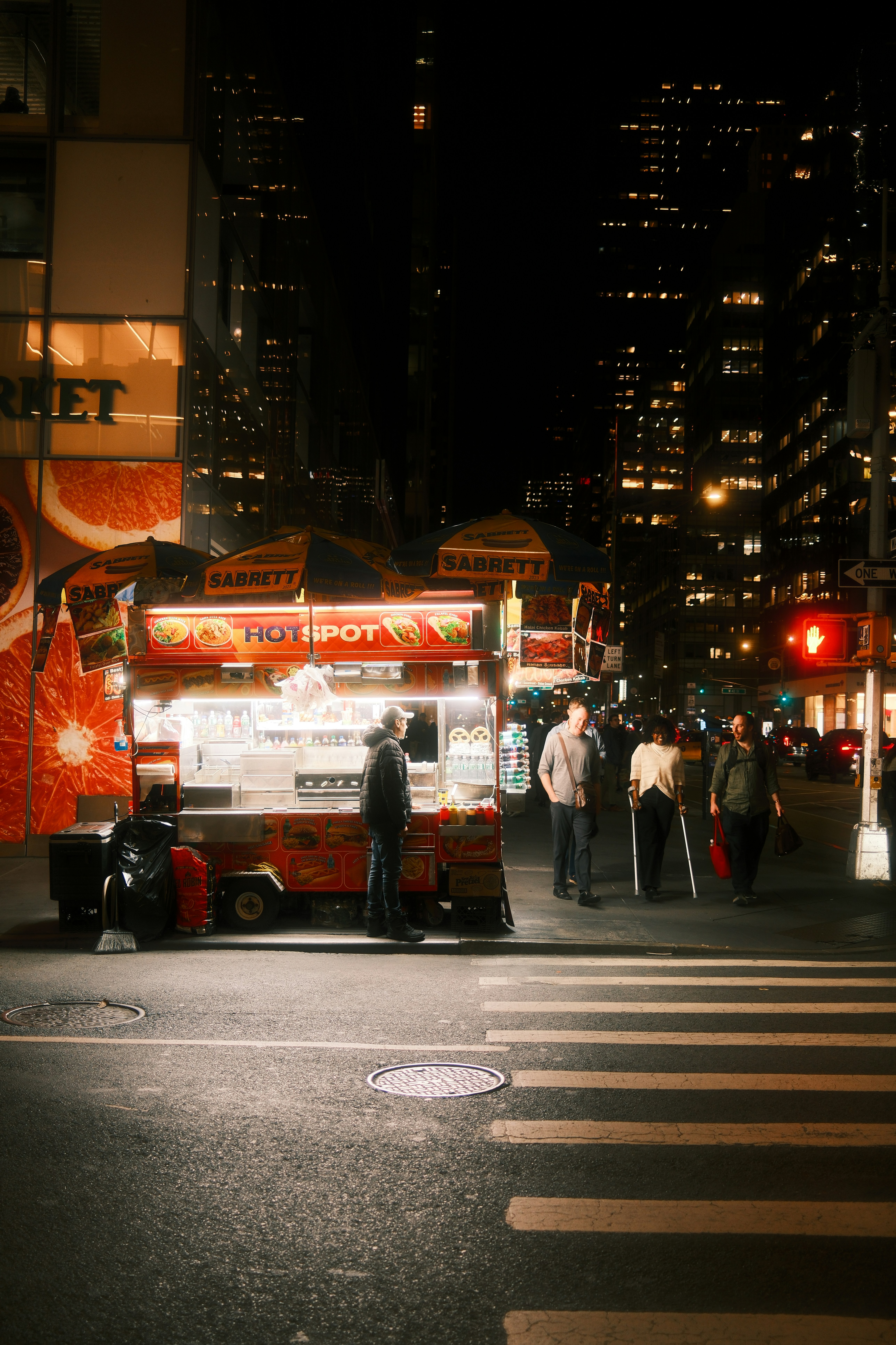 A food cart on a city street at night with people walking nearby