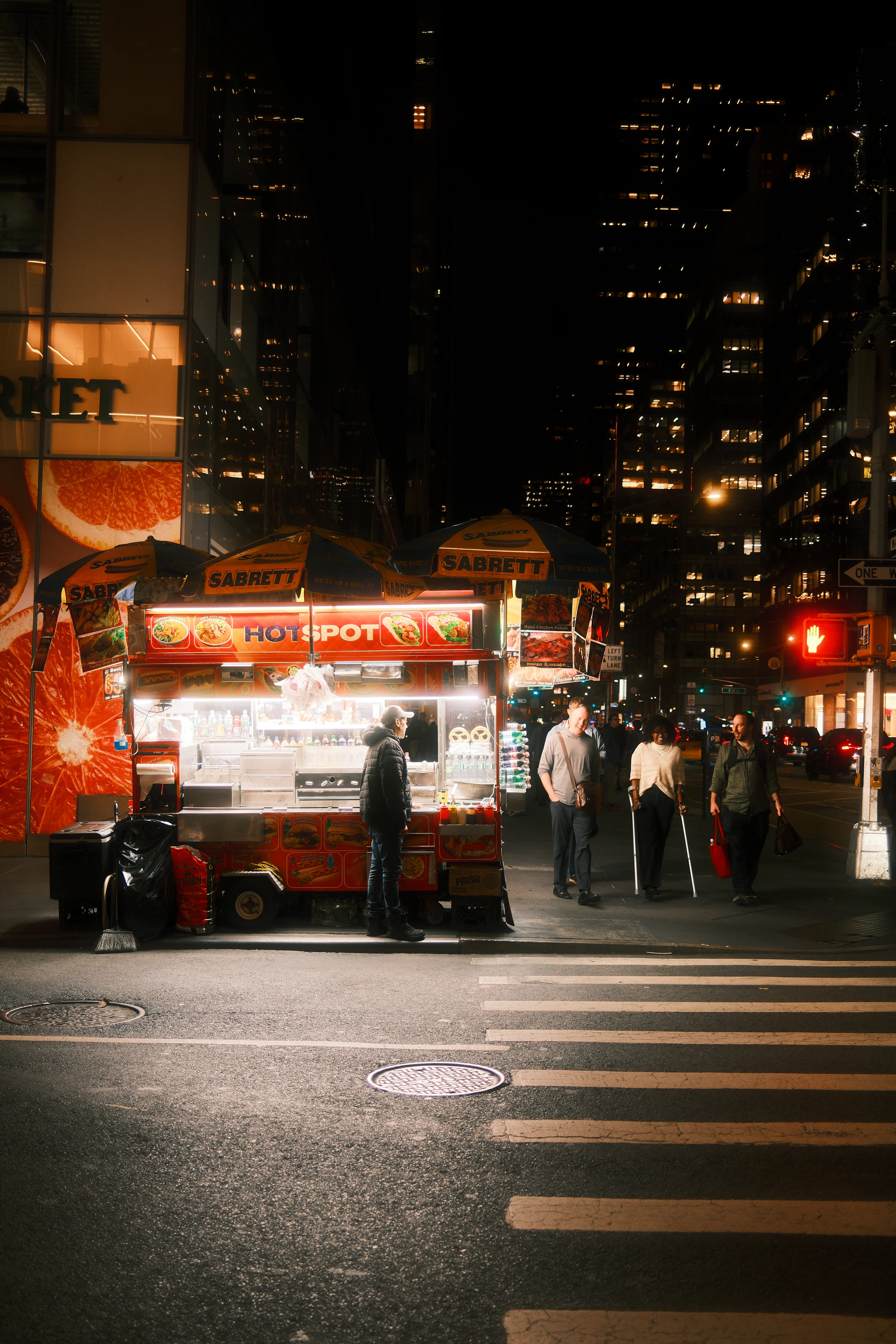 A food cart on a city street at night with people walking nearby