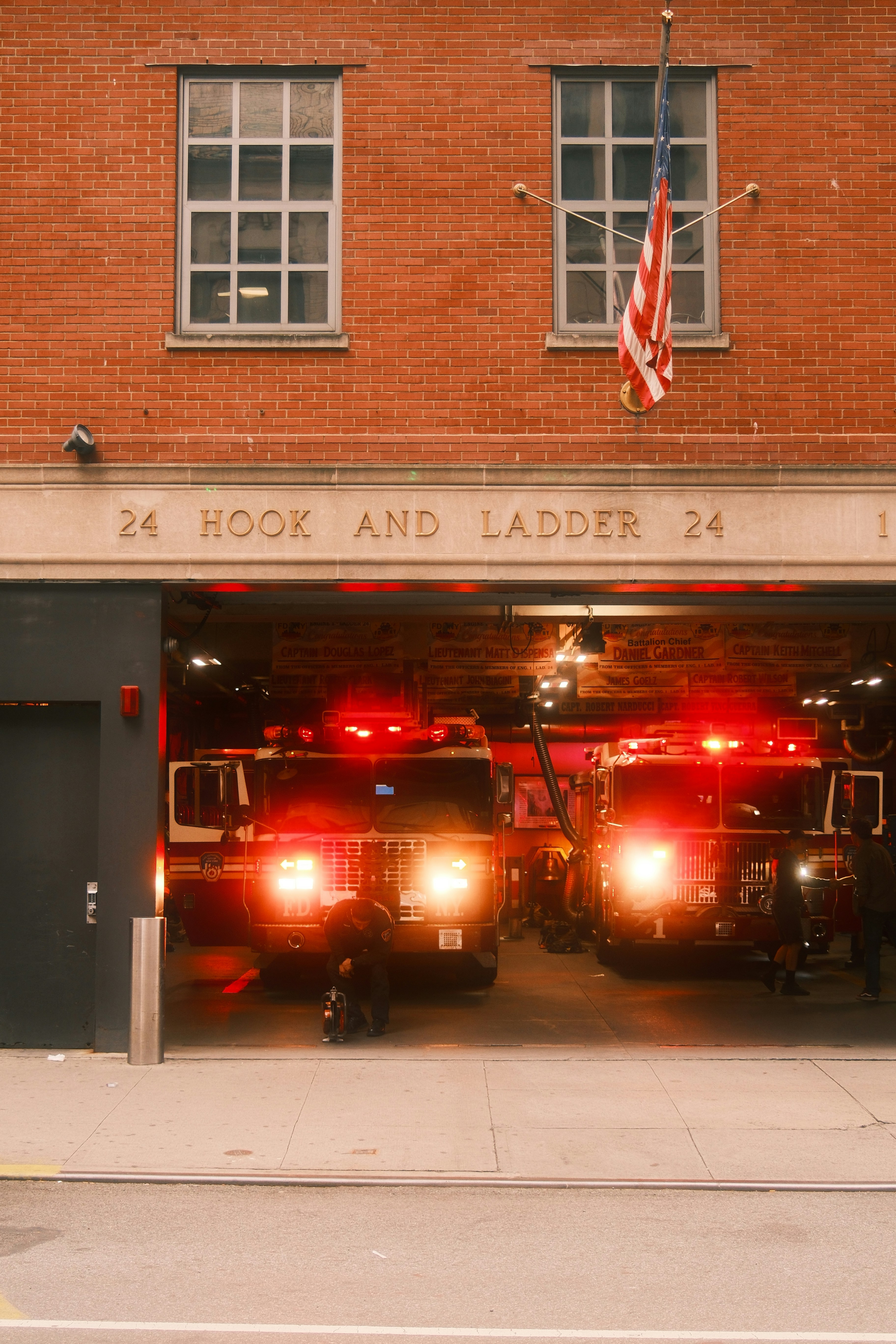 Two fire trucks with glowing headlights inside a brick fire station in New York
