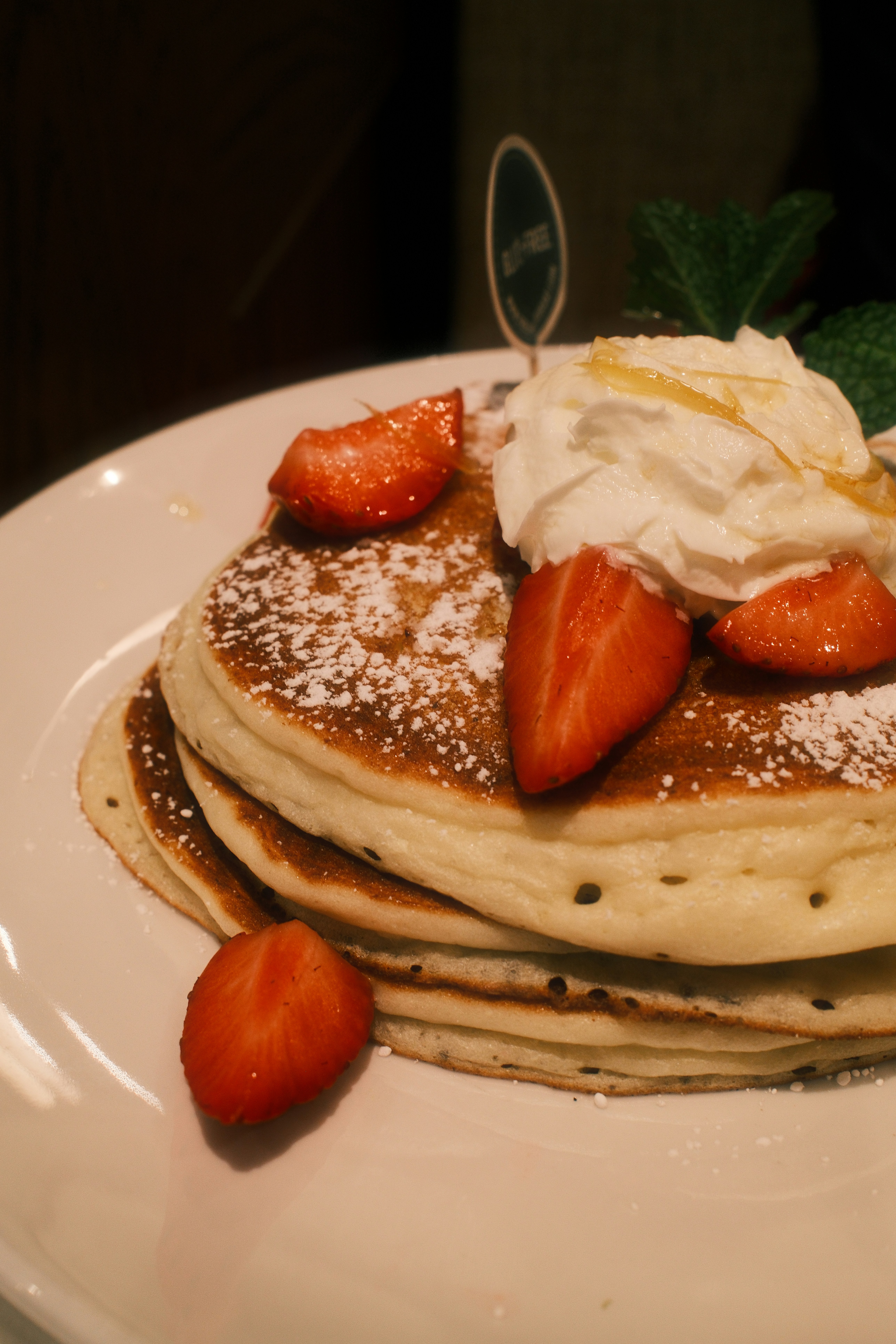A stack of pancakes topped with whipped cream and fresh strawberries on a plate
