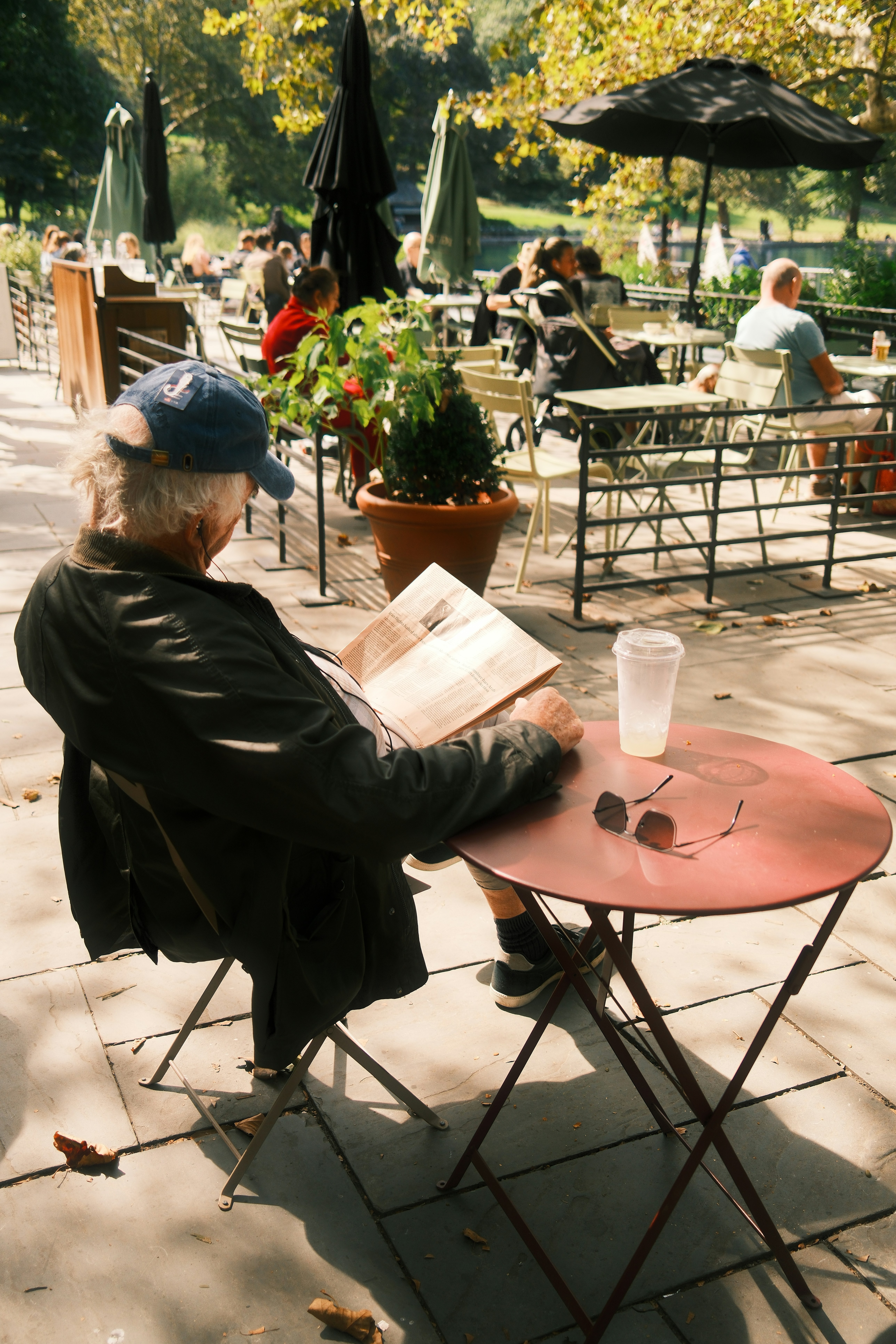 An older man in a blue cap reading a newspaper at a cafe table