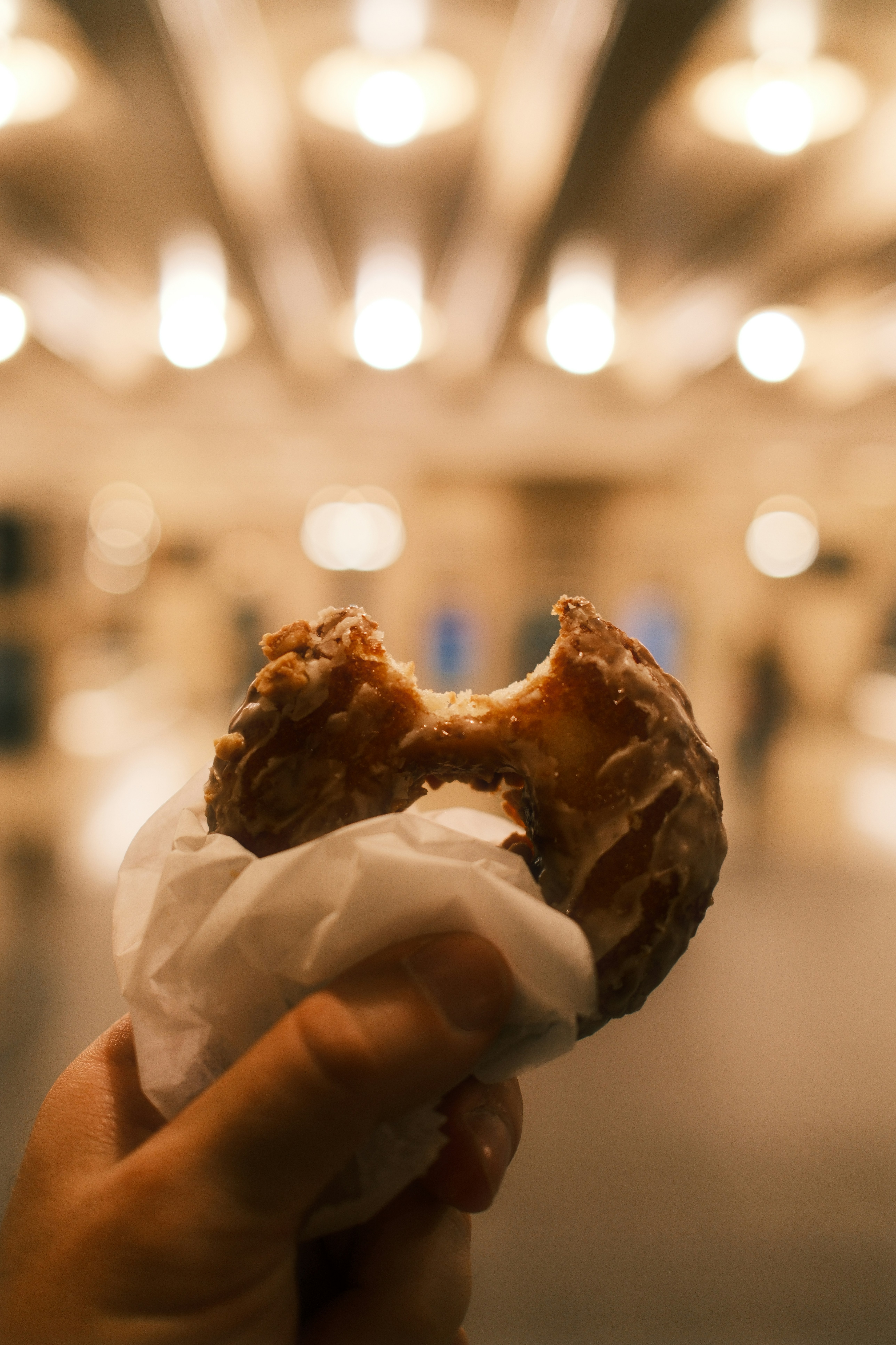 A hand holding a glazed donut with a bite taken out of it