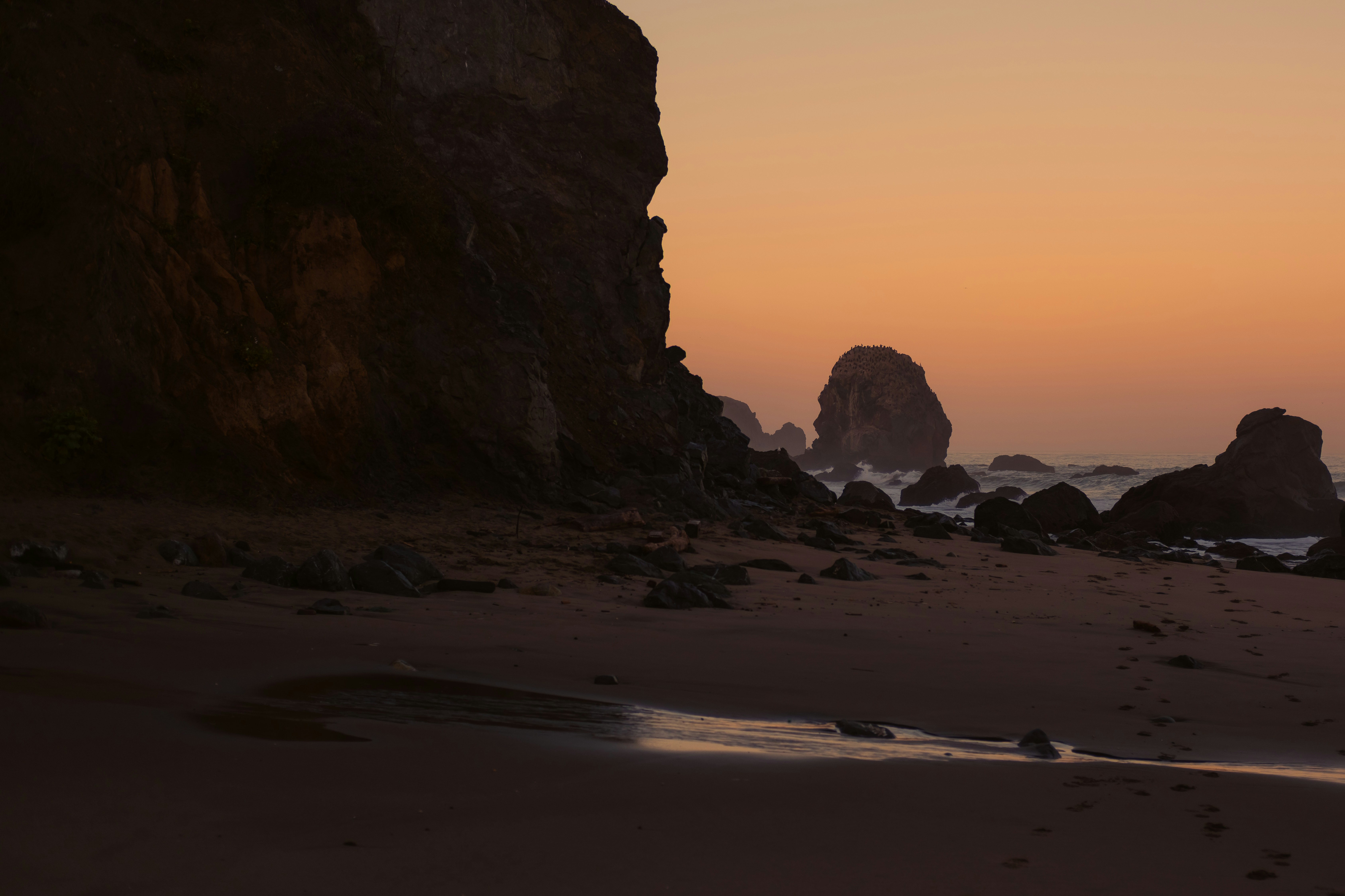 Rocky sea stacks along a sandy beach under a warm orange sky in San Francisco