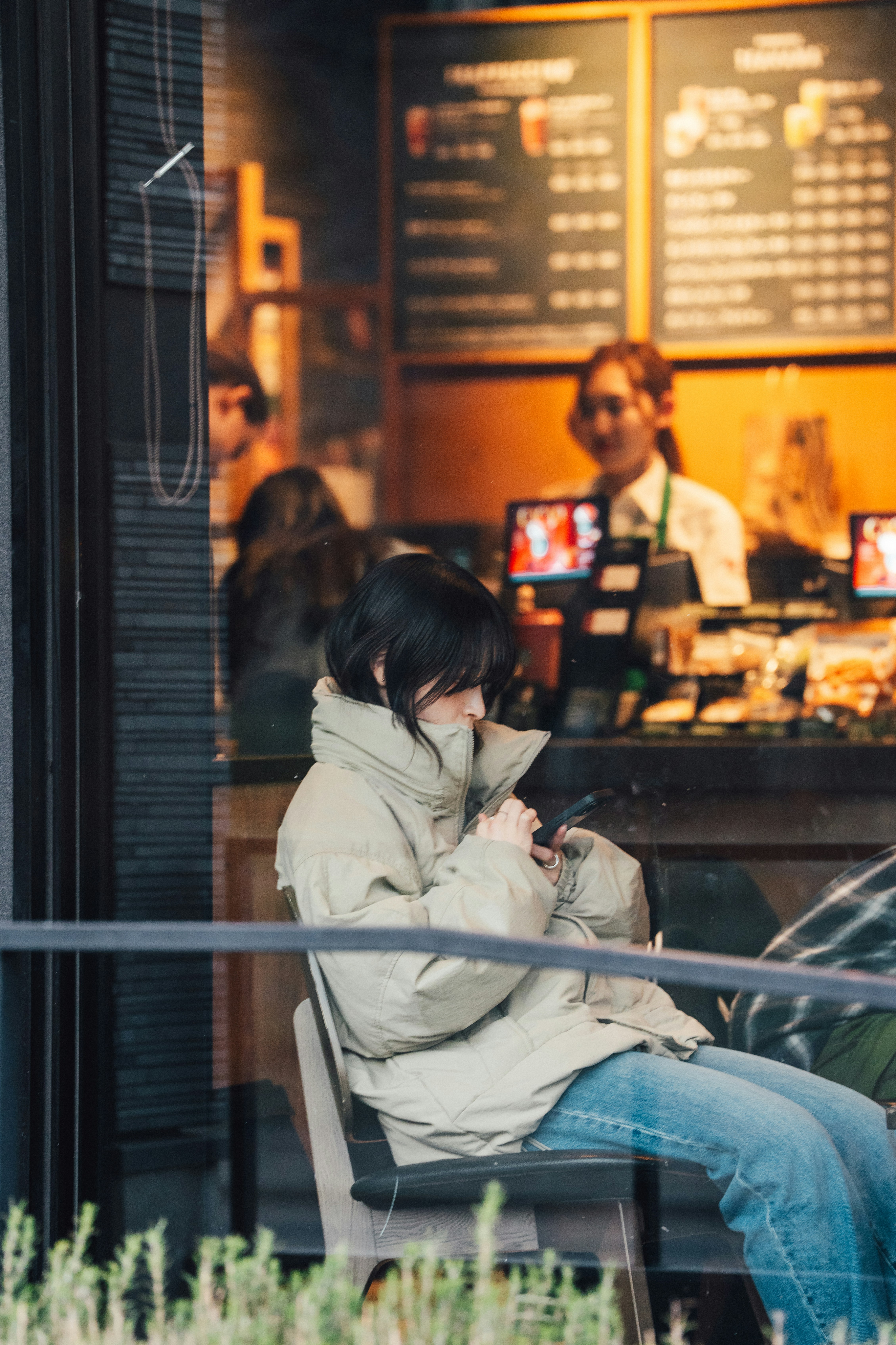 Une personne en doudoune beige utilisant un smartphone dans un café