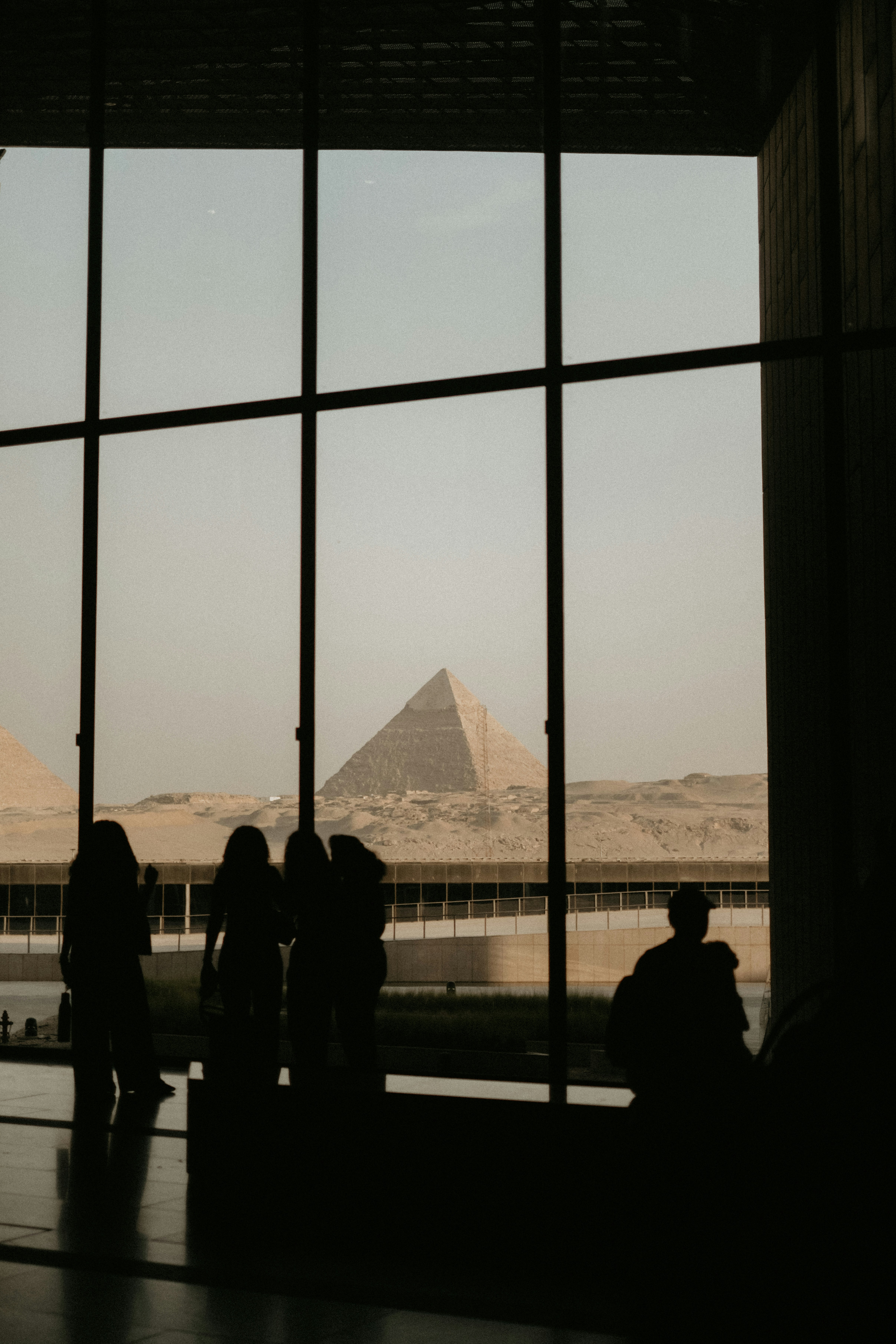Silhouettes of people looking through a large window at the Great Pyramids of Giza