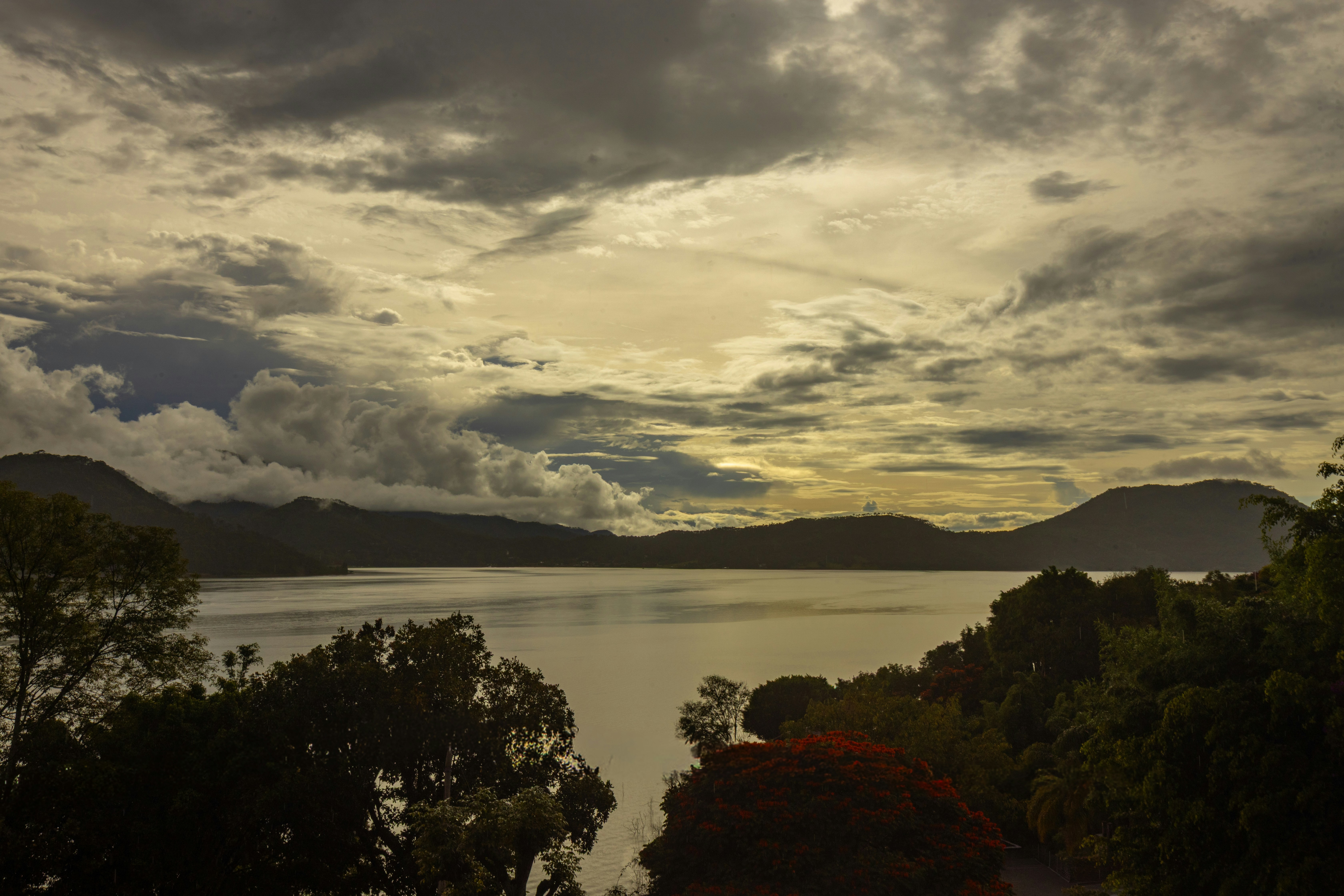 Um amplo lago cercado por montanhas sob um céu nublado com luz dourada