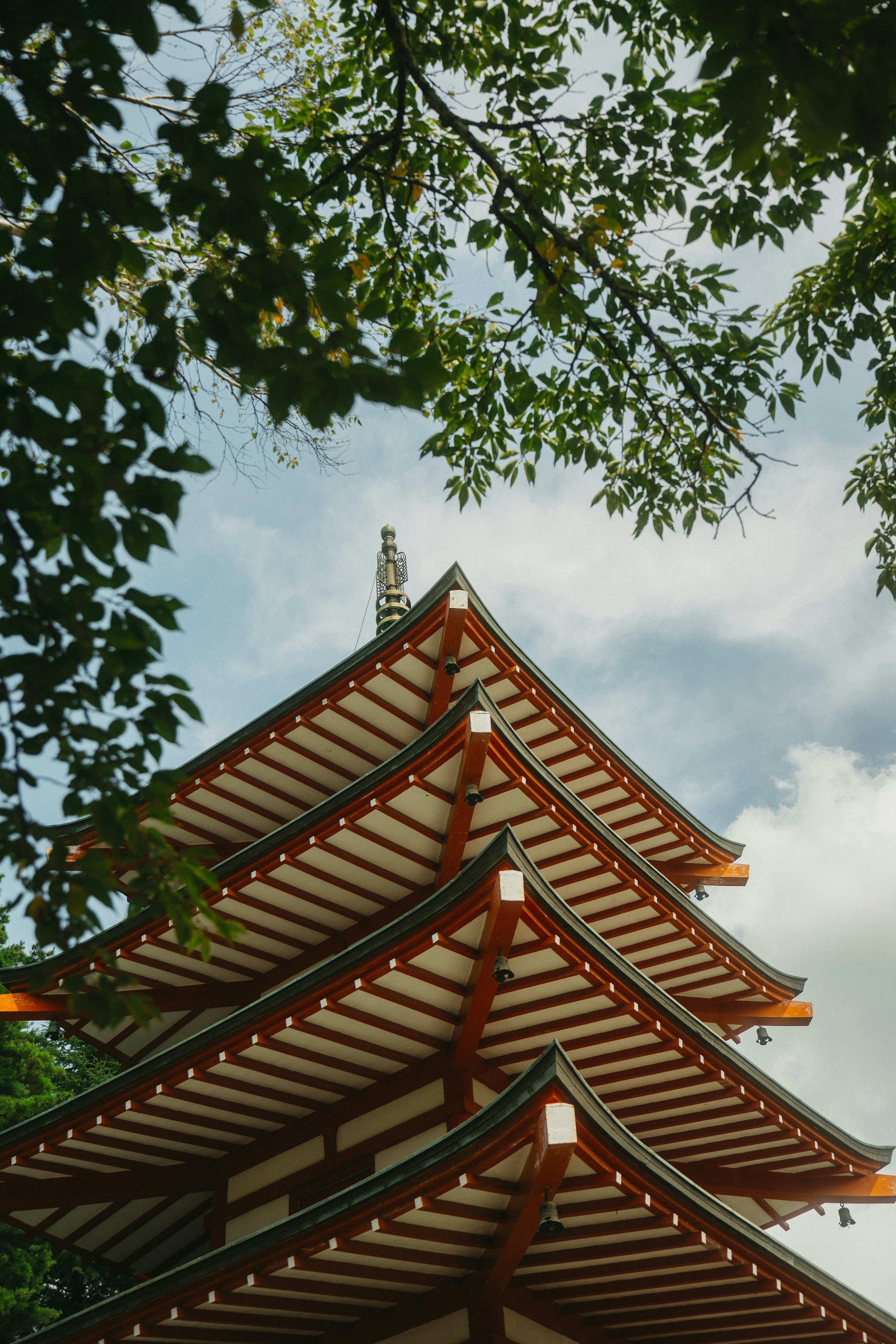 A multi-tiered orange pagoda roof framed by green tree branches against a blue sky