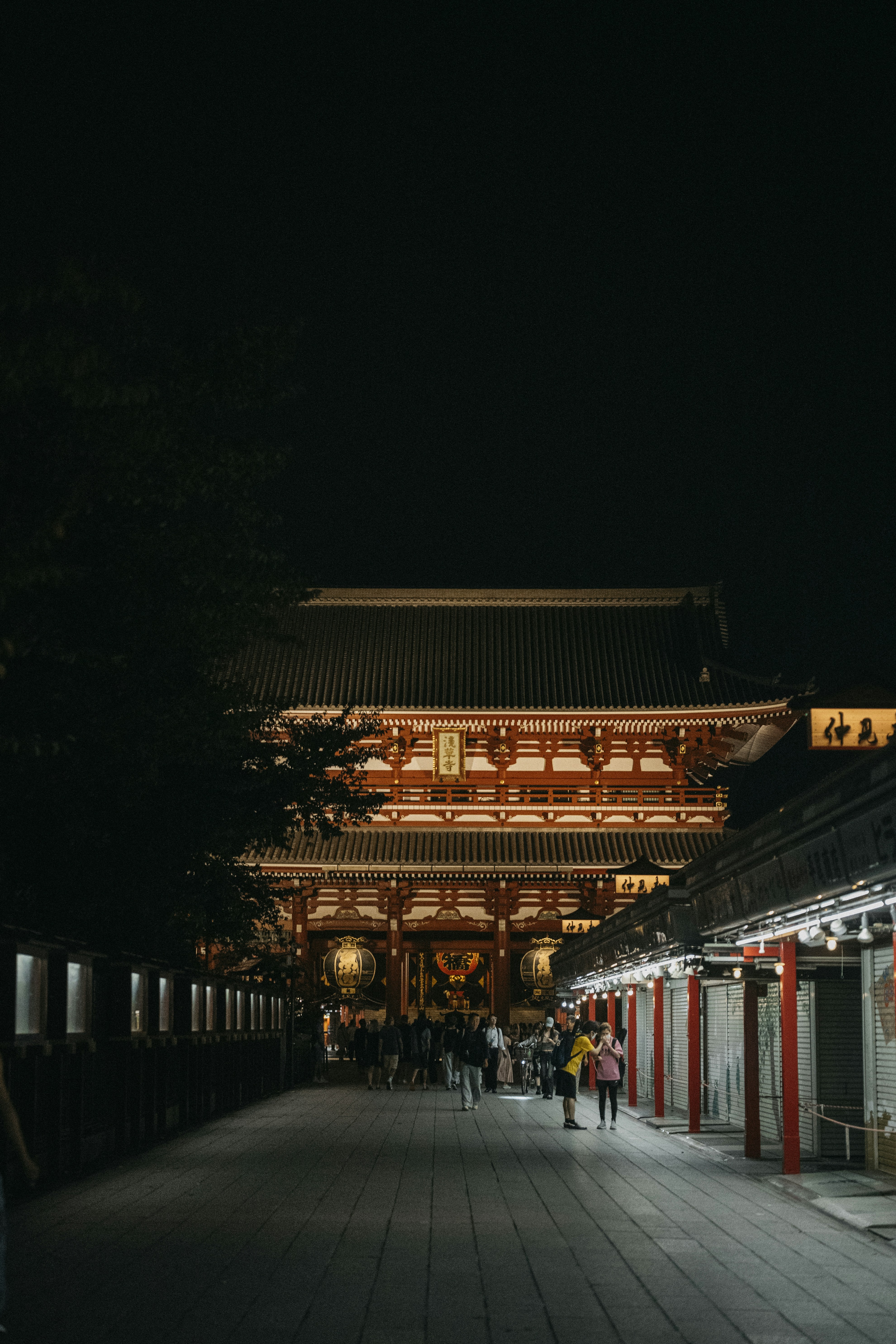 People walking on a stone path toward the illuminated Senso-ji temple gate in Tokyo
