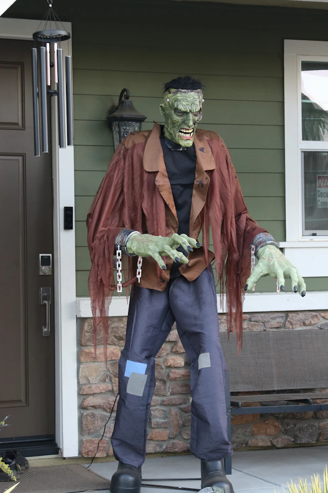 A green-skinned Frankenstein's monster figure with chains on its wrists standing on a porch