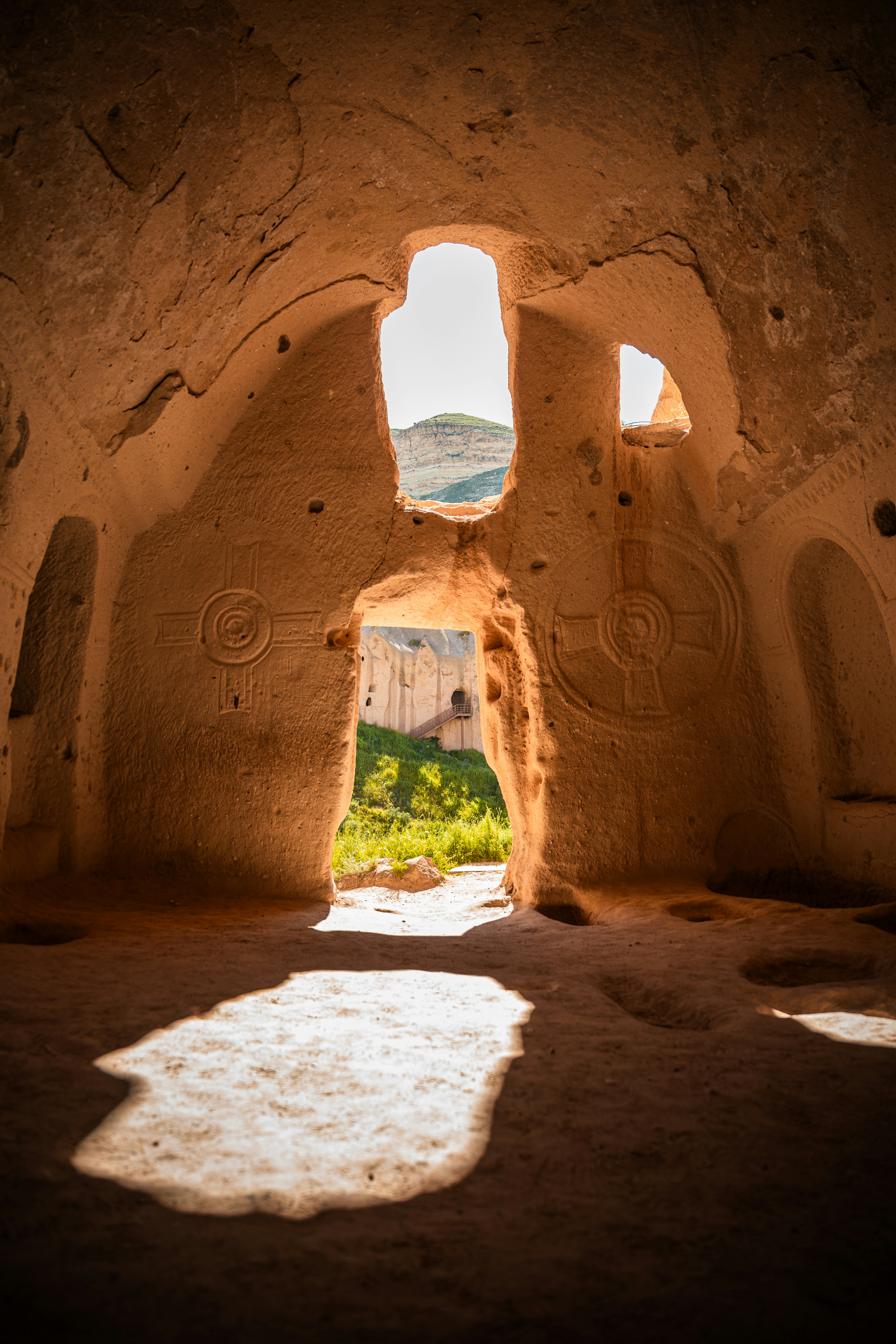 Carved stone interior with circular reliefs looking out to a green valley in Cappadocia