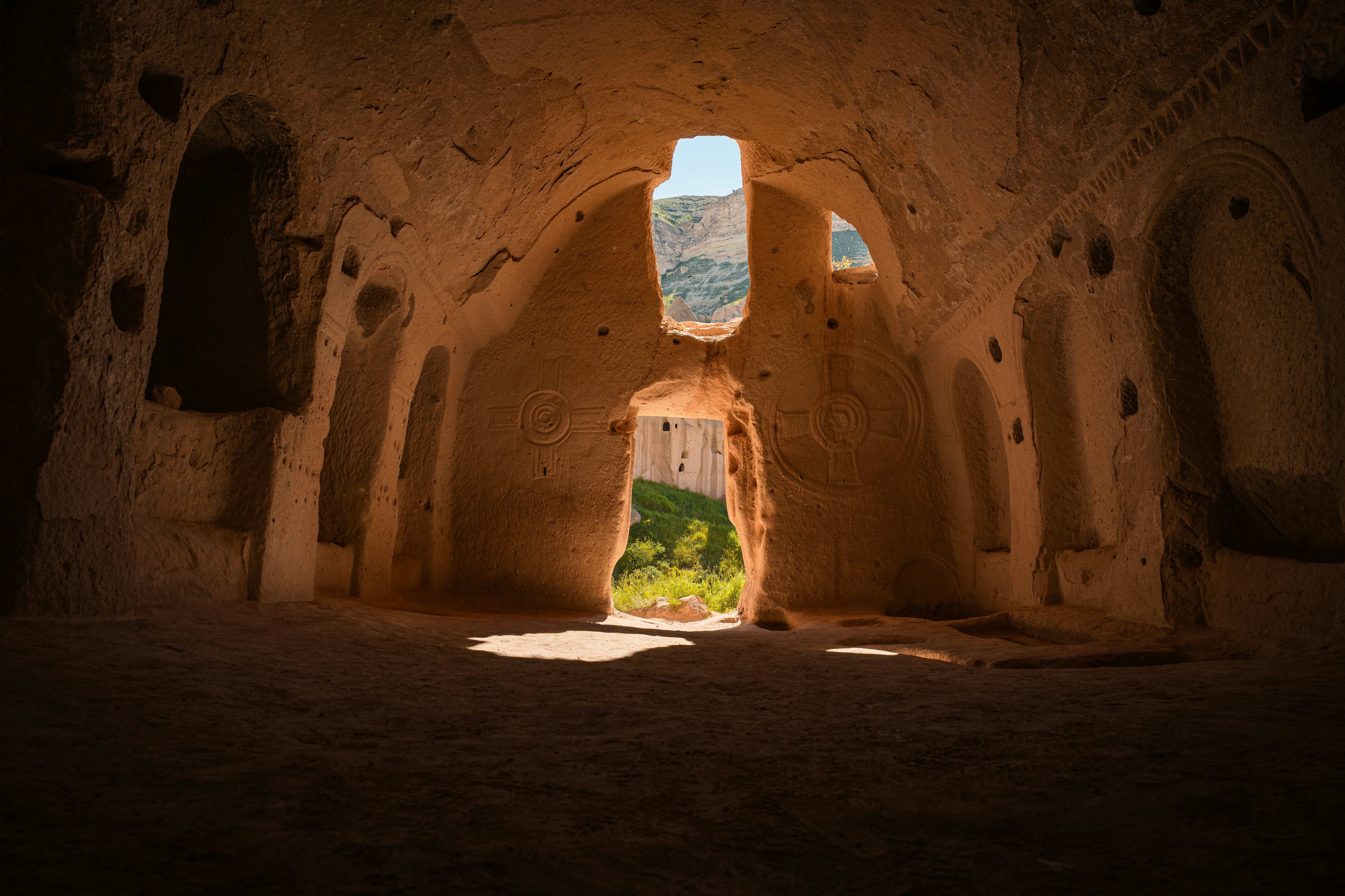 A carved stone cave interior with circular symbols looking out to a green valley