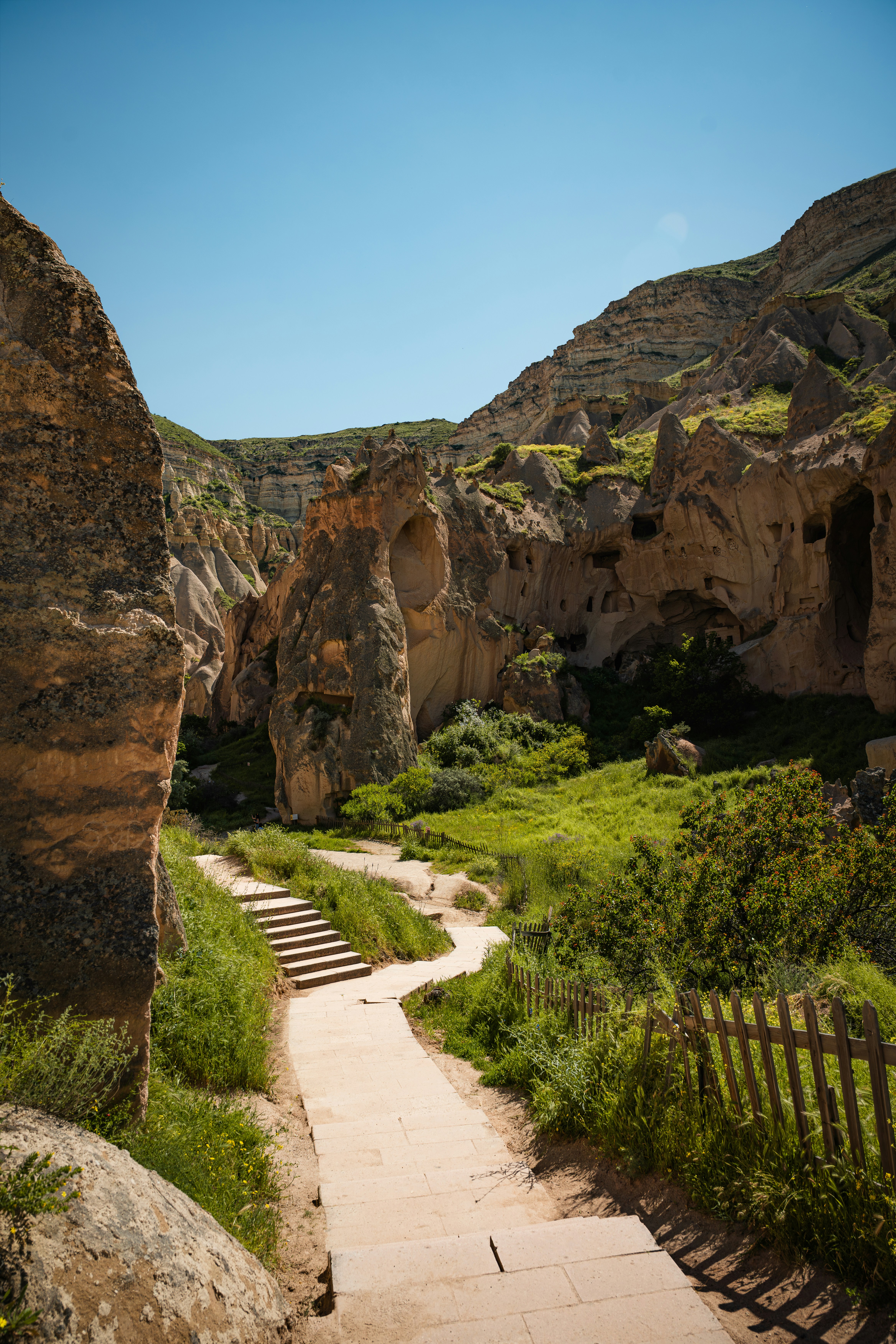 A stone path winding through a green valley with tall rock formations in Cappadocia
