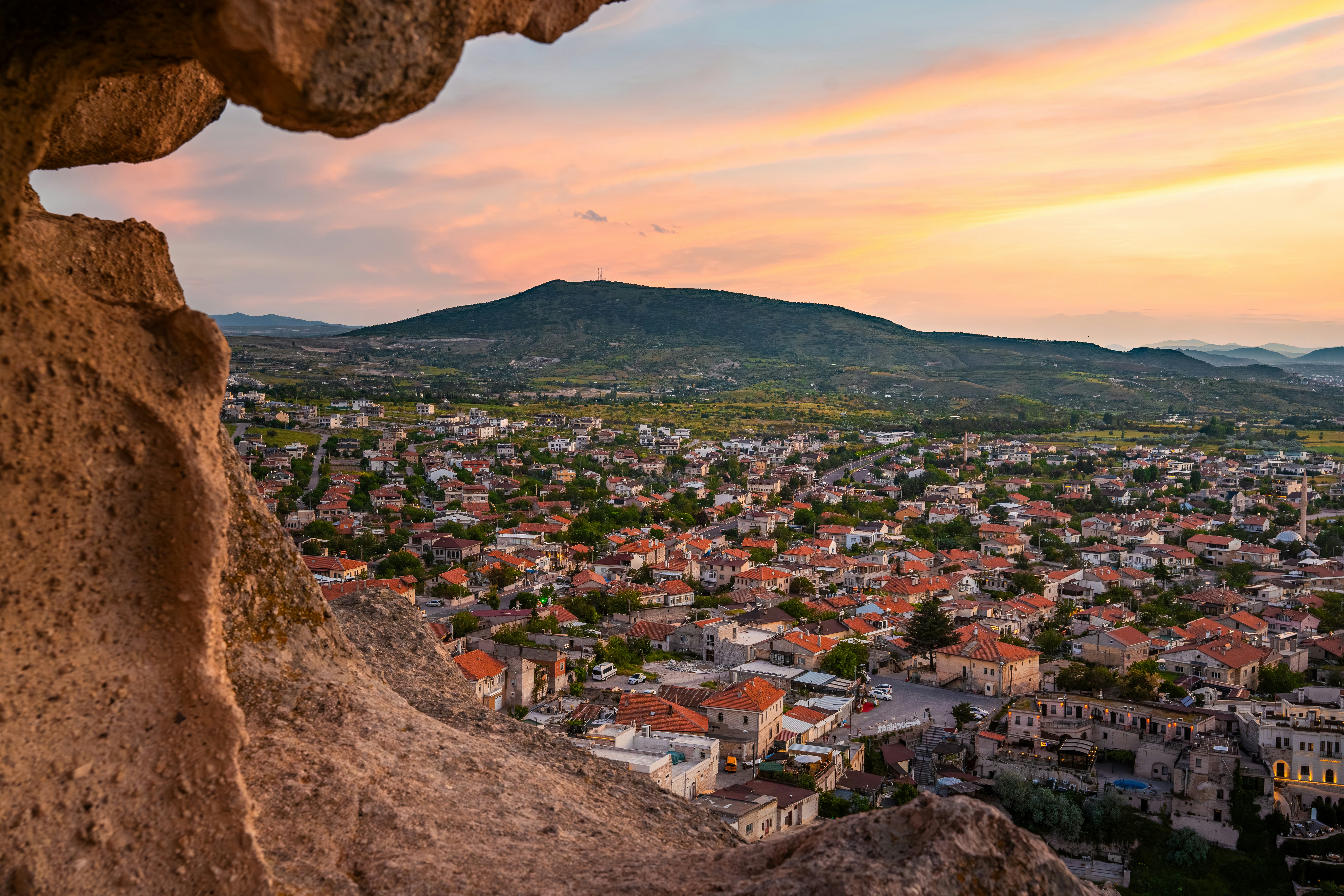A town with red-tiled roofs nestled in a valley under a warm orange sky