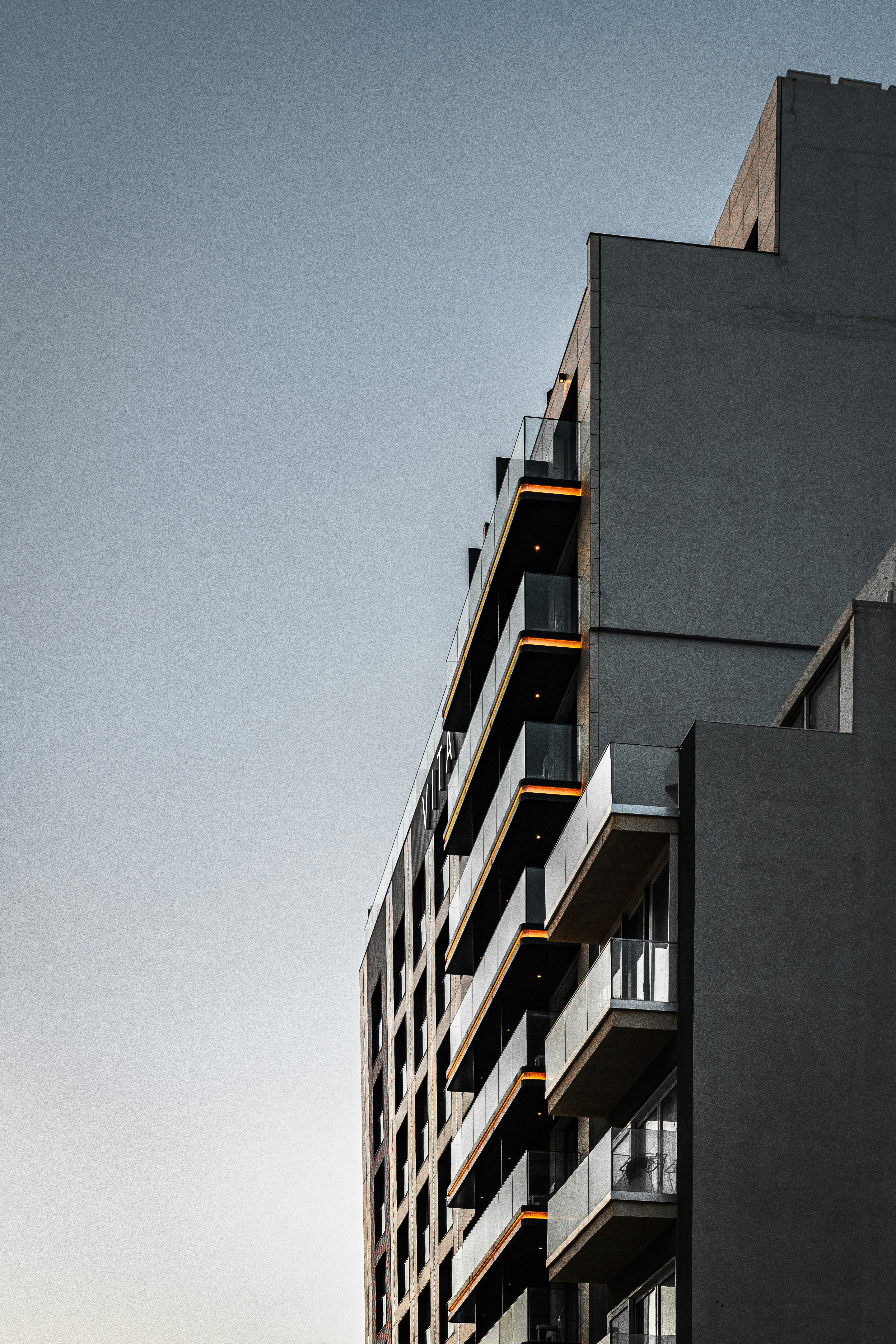 A modern apartment building with glass balconies illuminated by warm orange lights at dusk