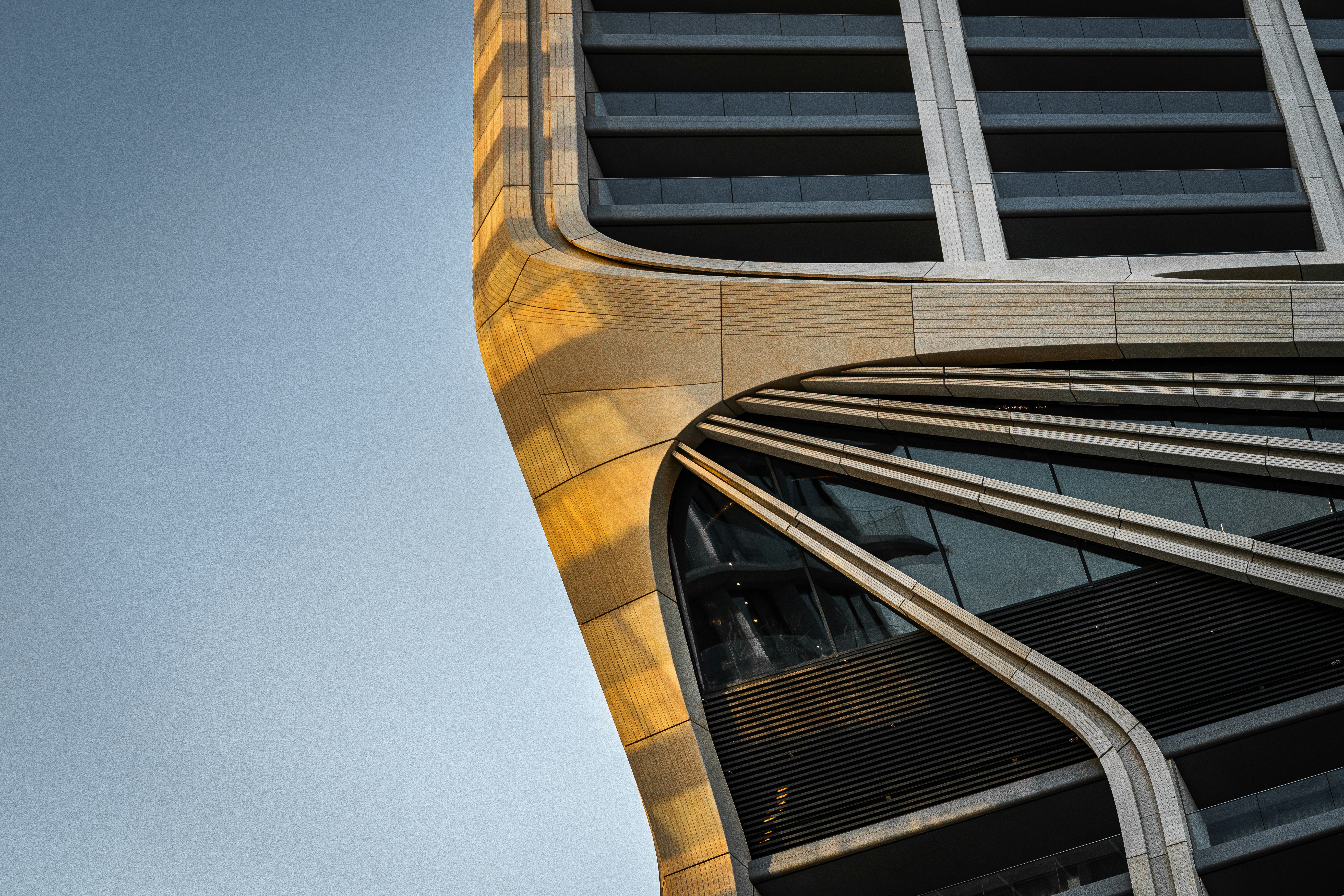 Curved beige facade of a modern skyscraper against a clear blue sky