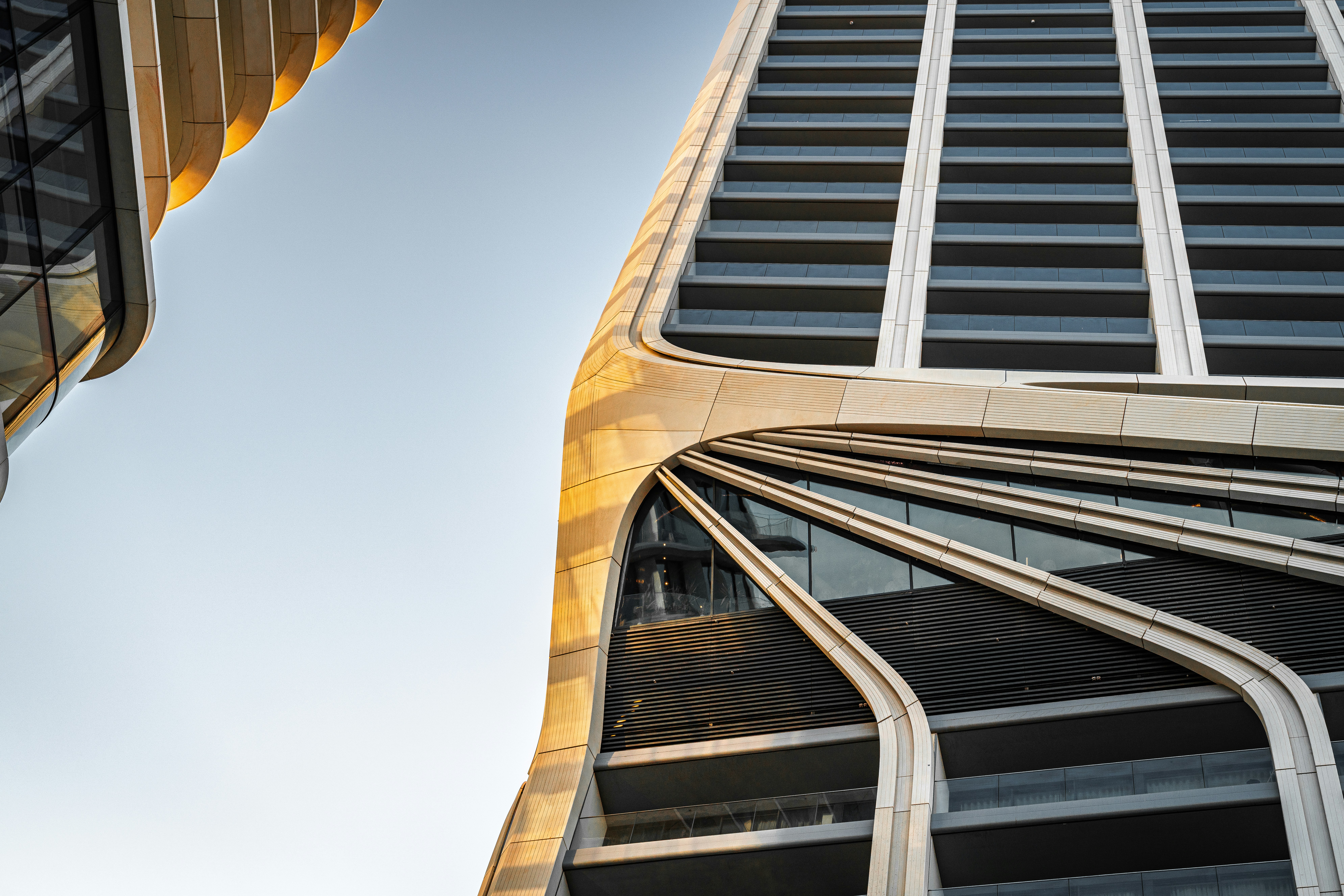 Curved beige facade of a modern skyscraper against a clear blue sky
