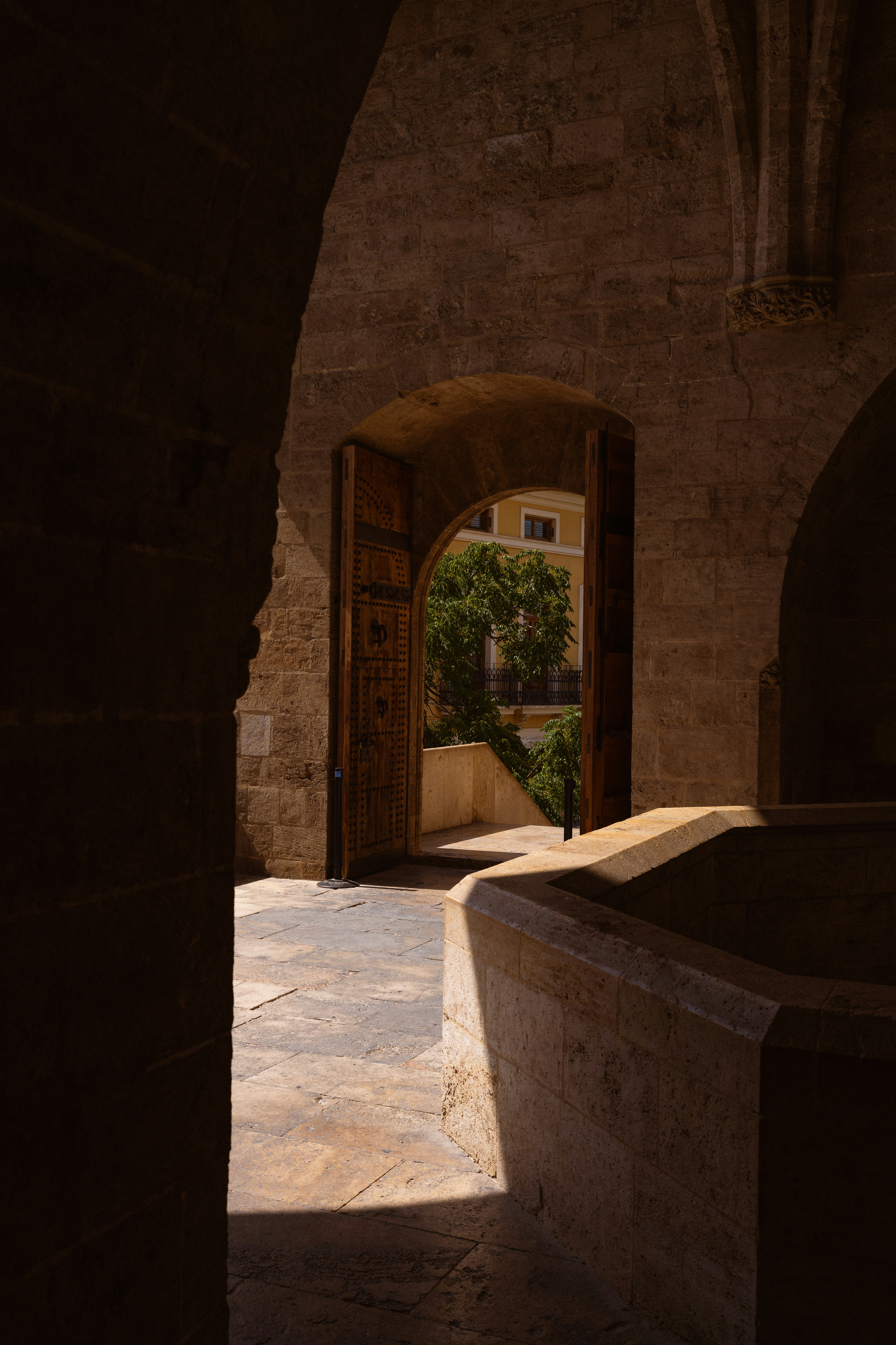 A stone archway framing a view of a sunlit courtyard and green tree