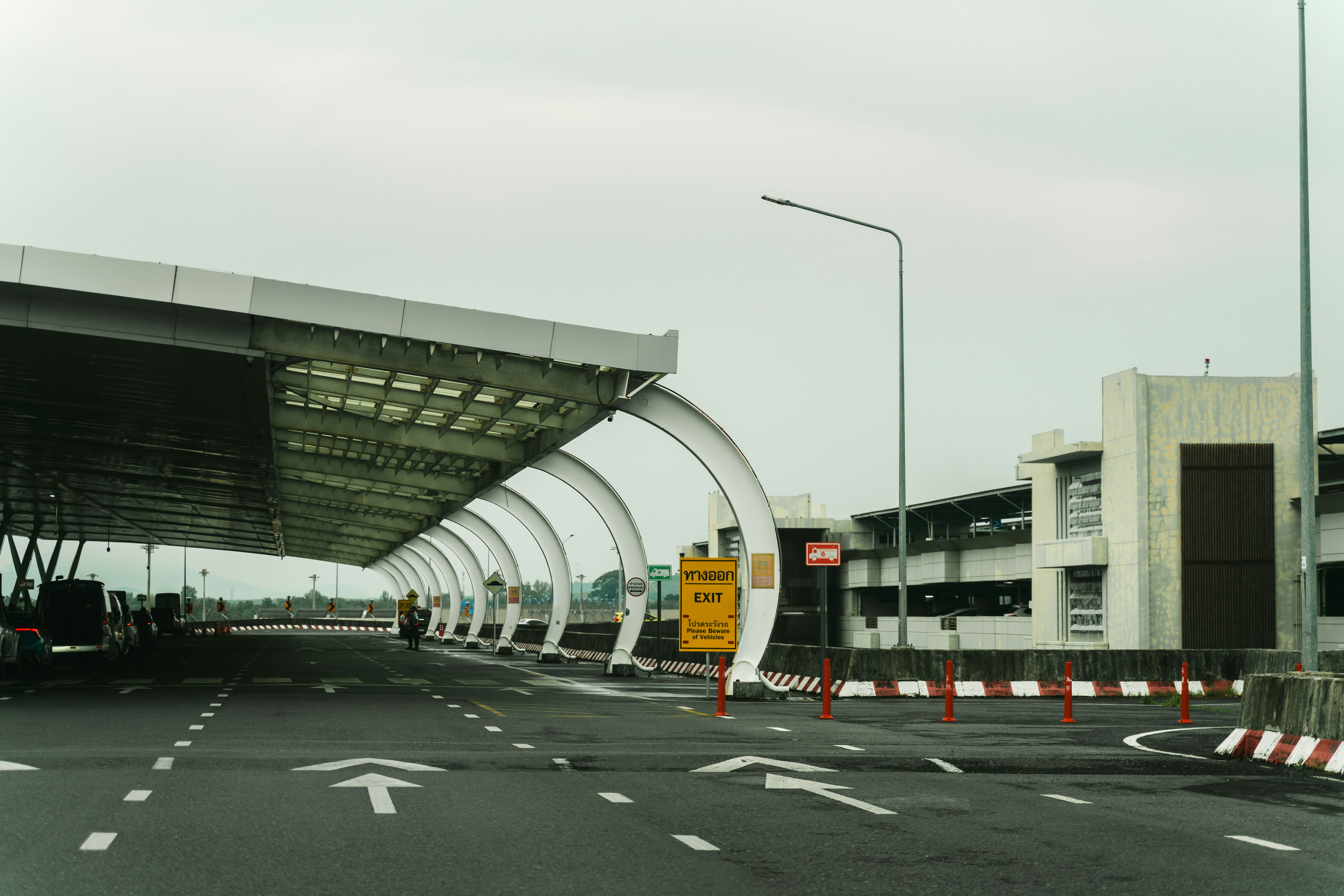 A road leading under a modern white canopy with a yellow exit sign