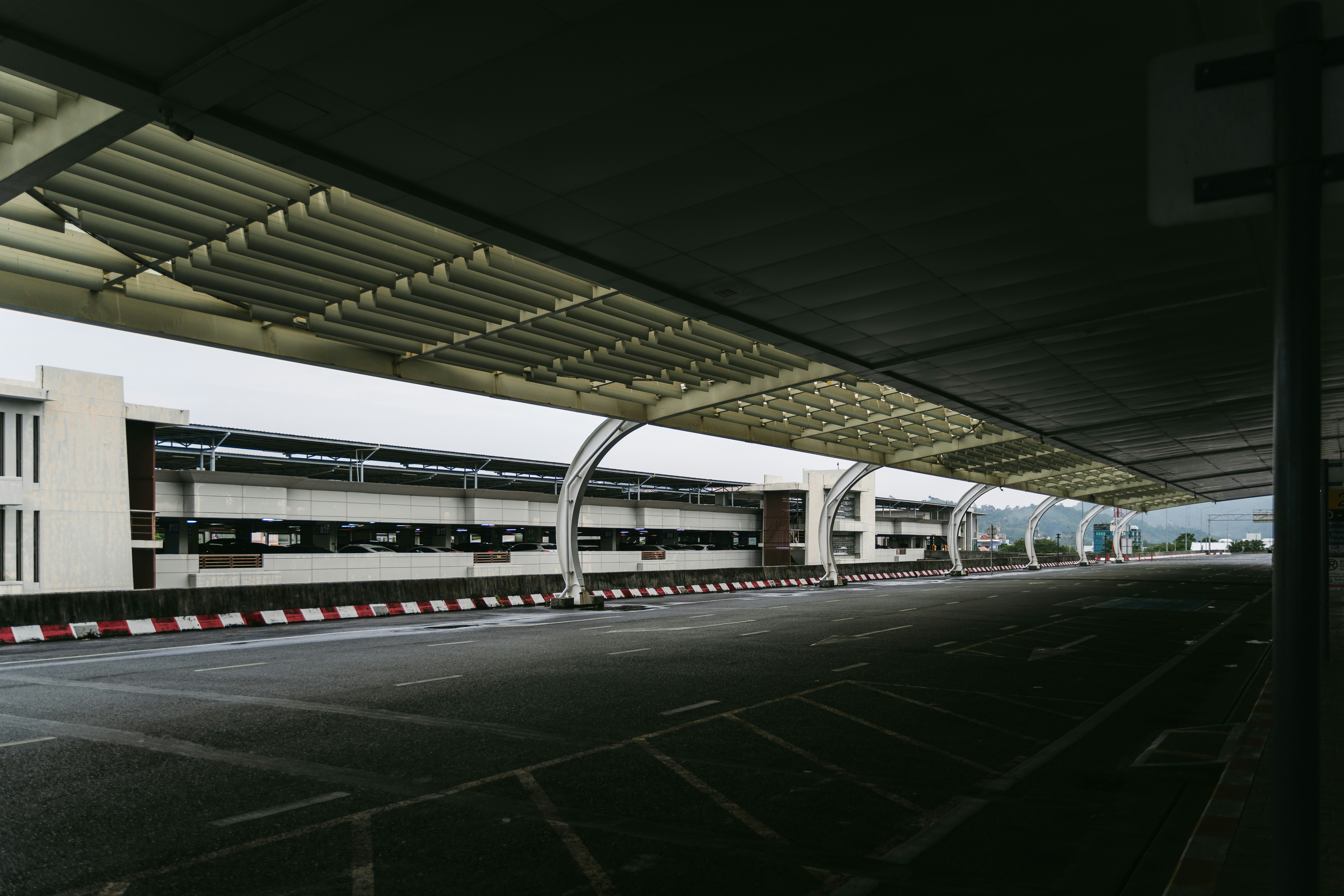An empty road beneath a long white canopy at a parking structure