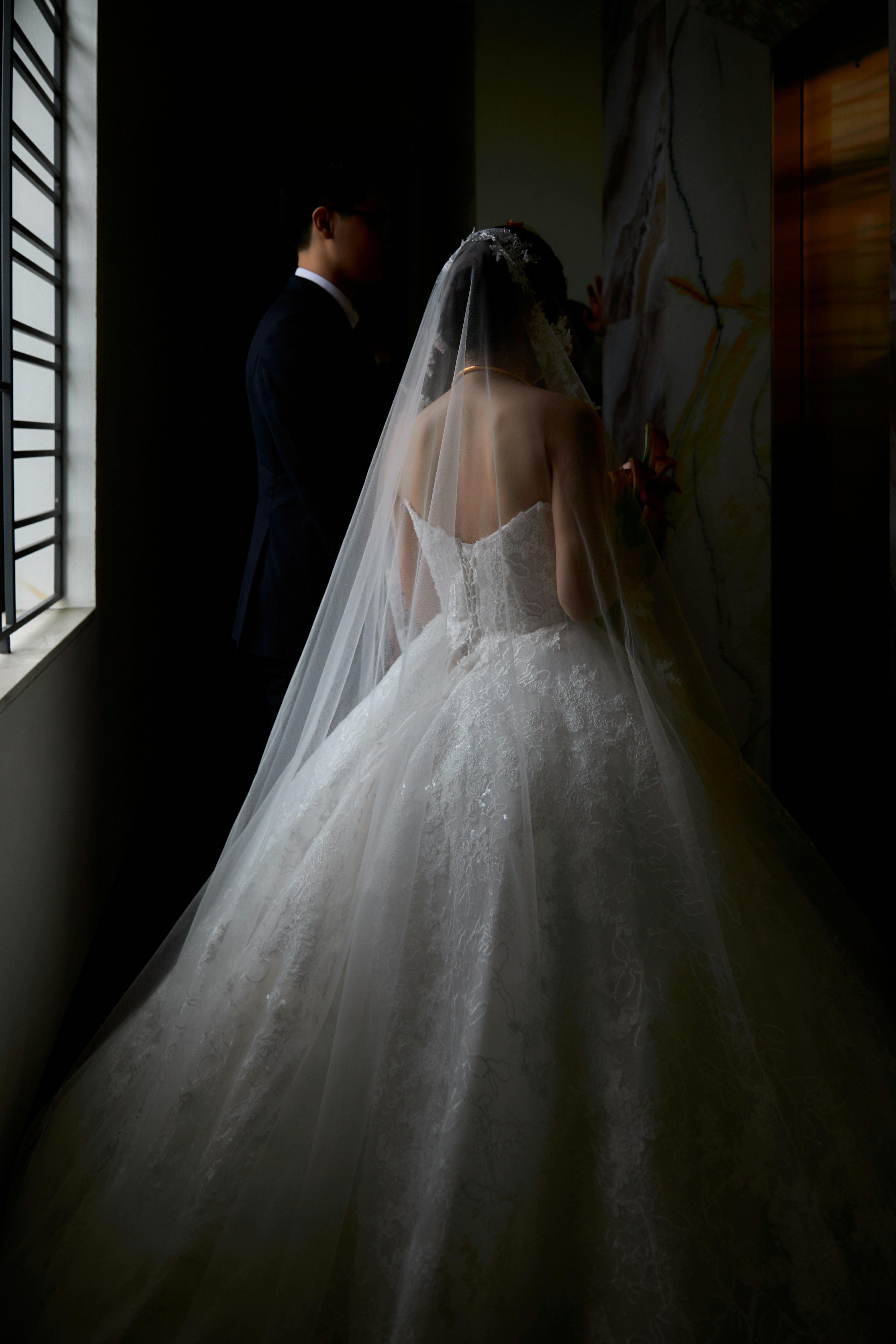 A bride in a white lace gown and veil beside a man in a suit