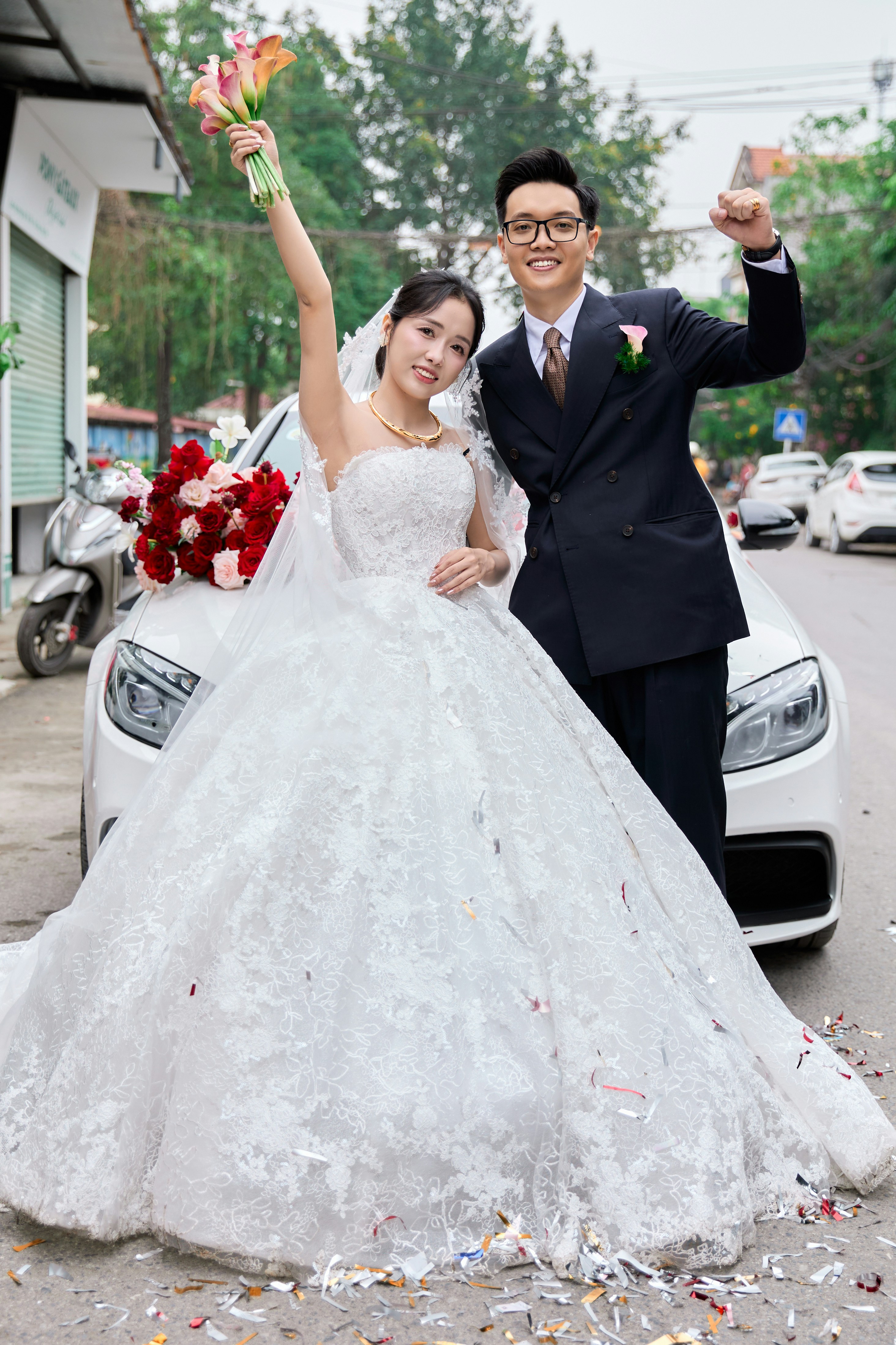 A bride and groom celebrating in front of a white car on a street