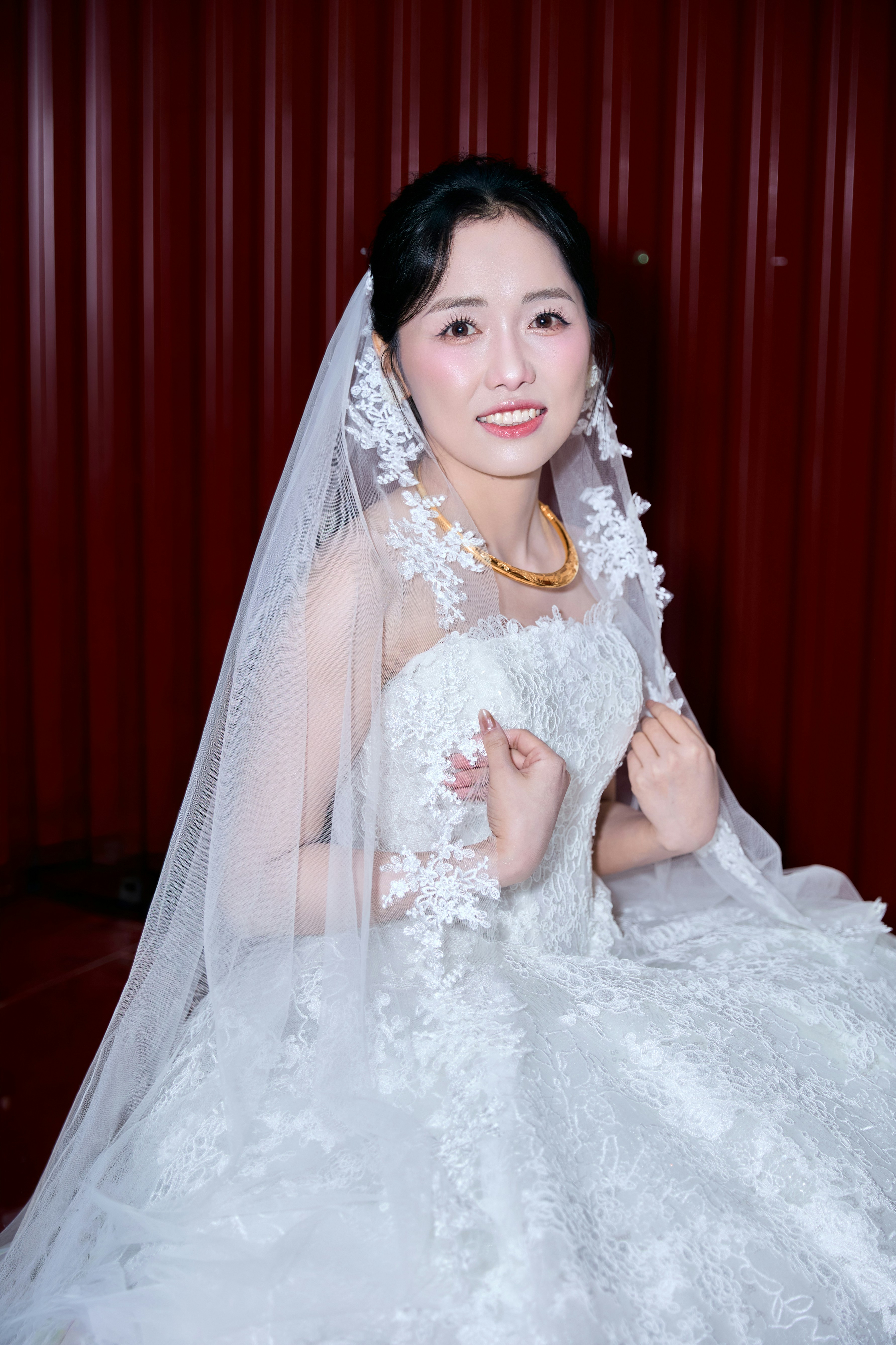A woman in a white lace wedding dress and veil against a red background