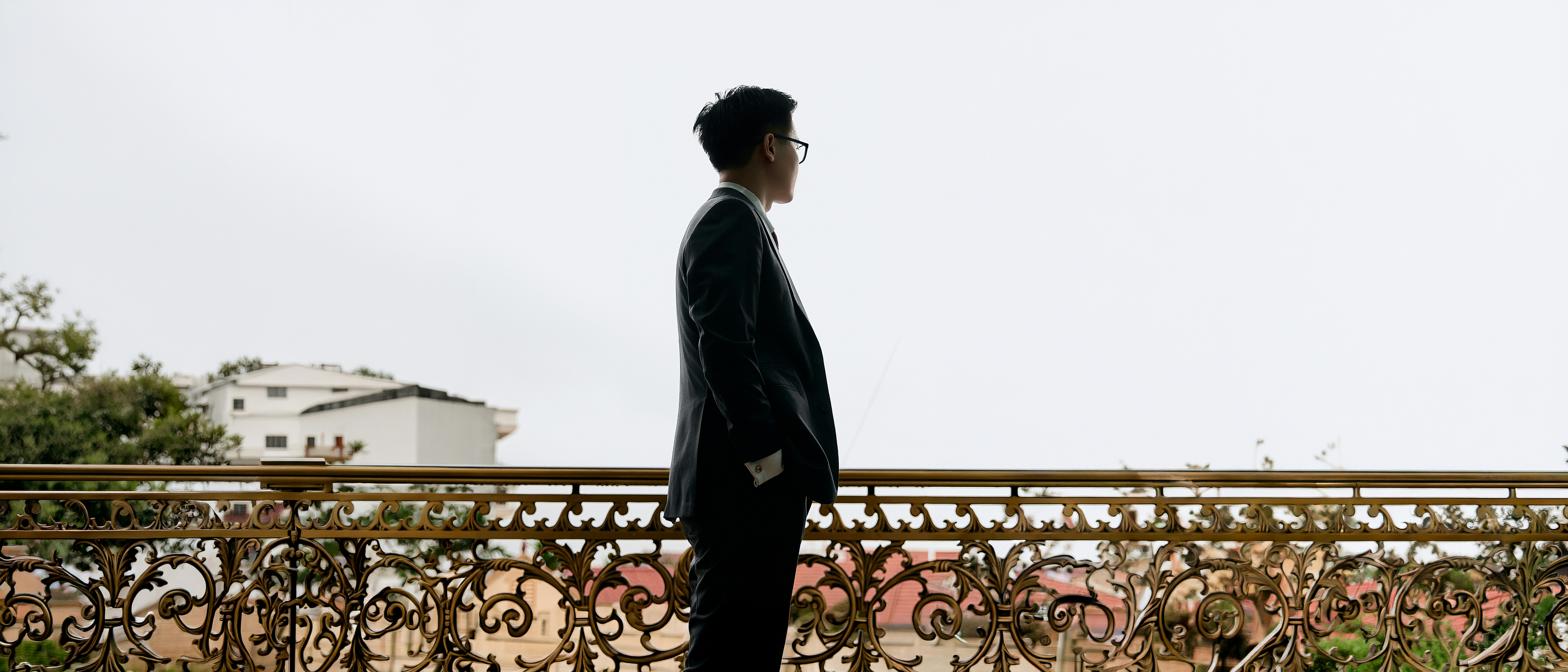 A man in a suit looking out from a balcony with ornate metal railings