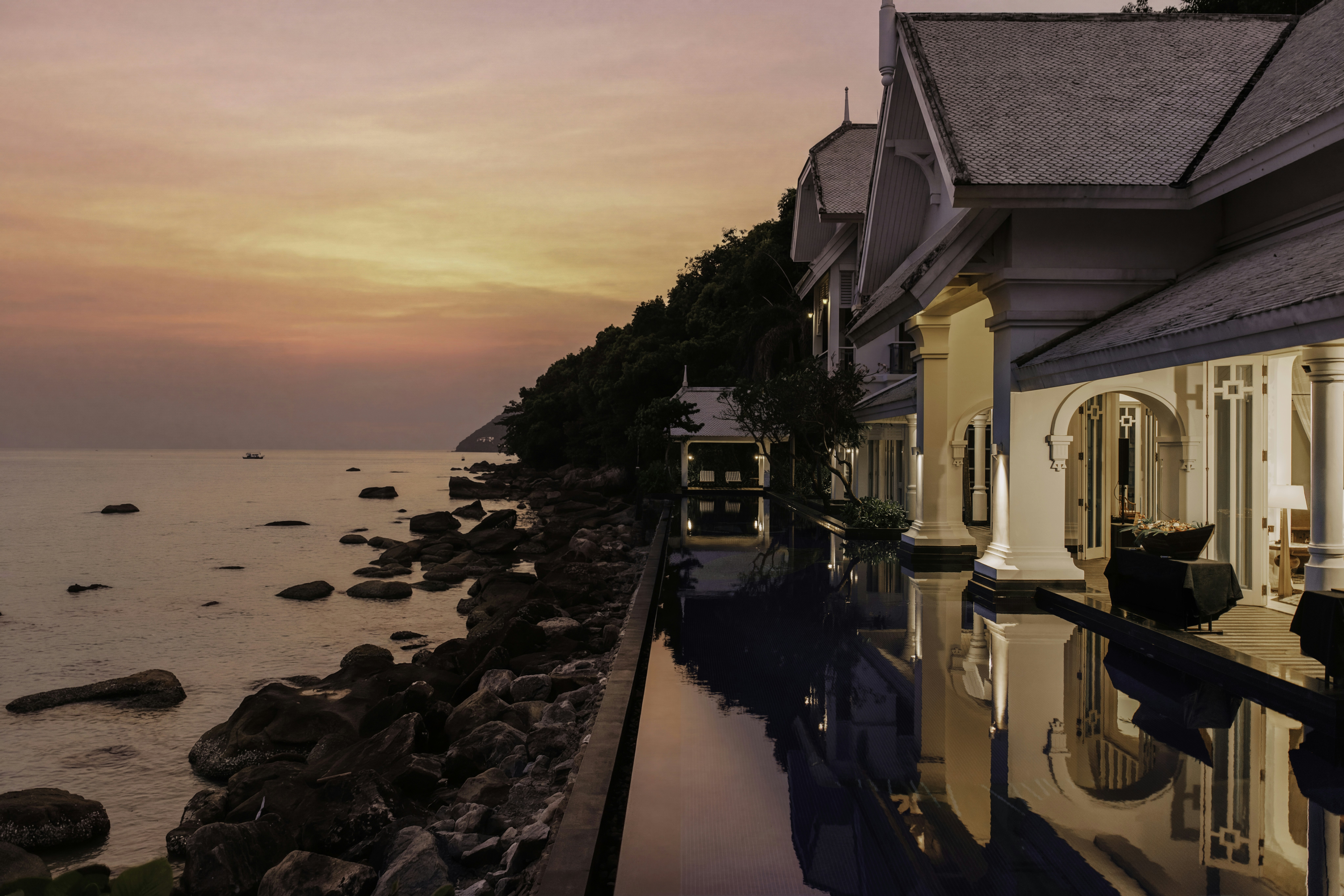 A luxury resort villa with an infinity pool overlooking a rocky coastline at golden hour