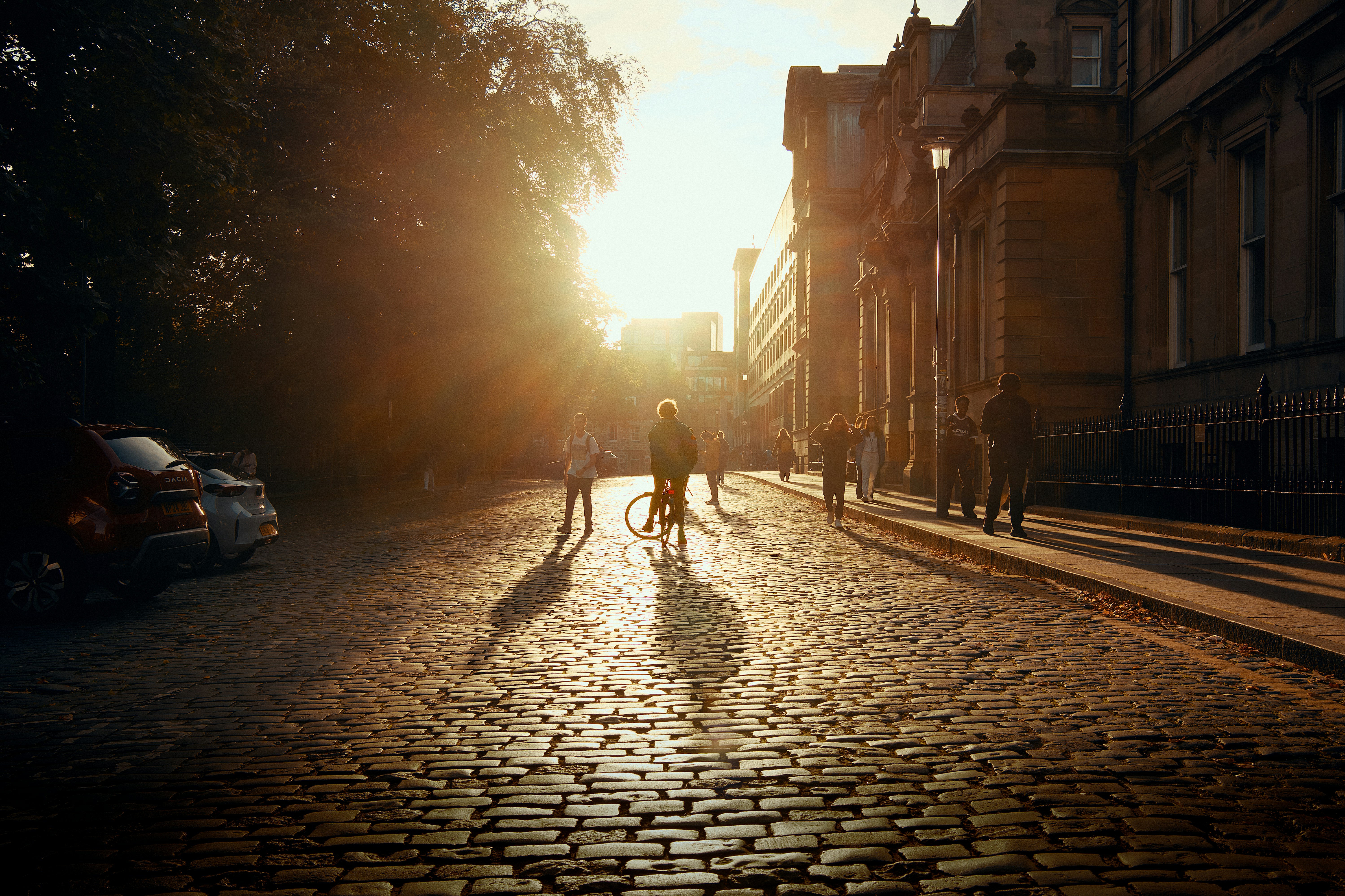 People walking and cycling on a cobblestone street during the golden hour