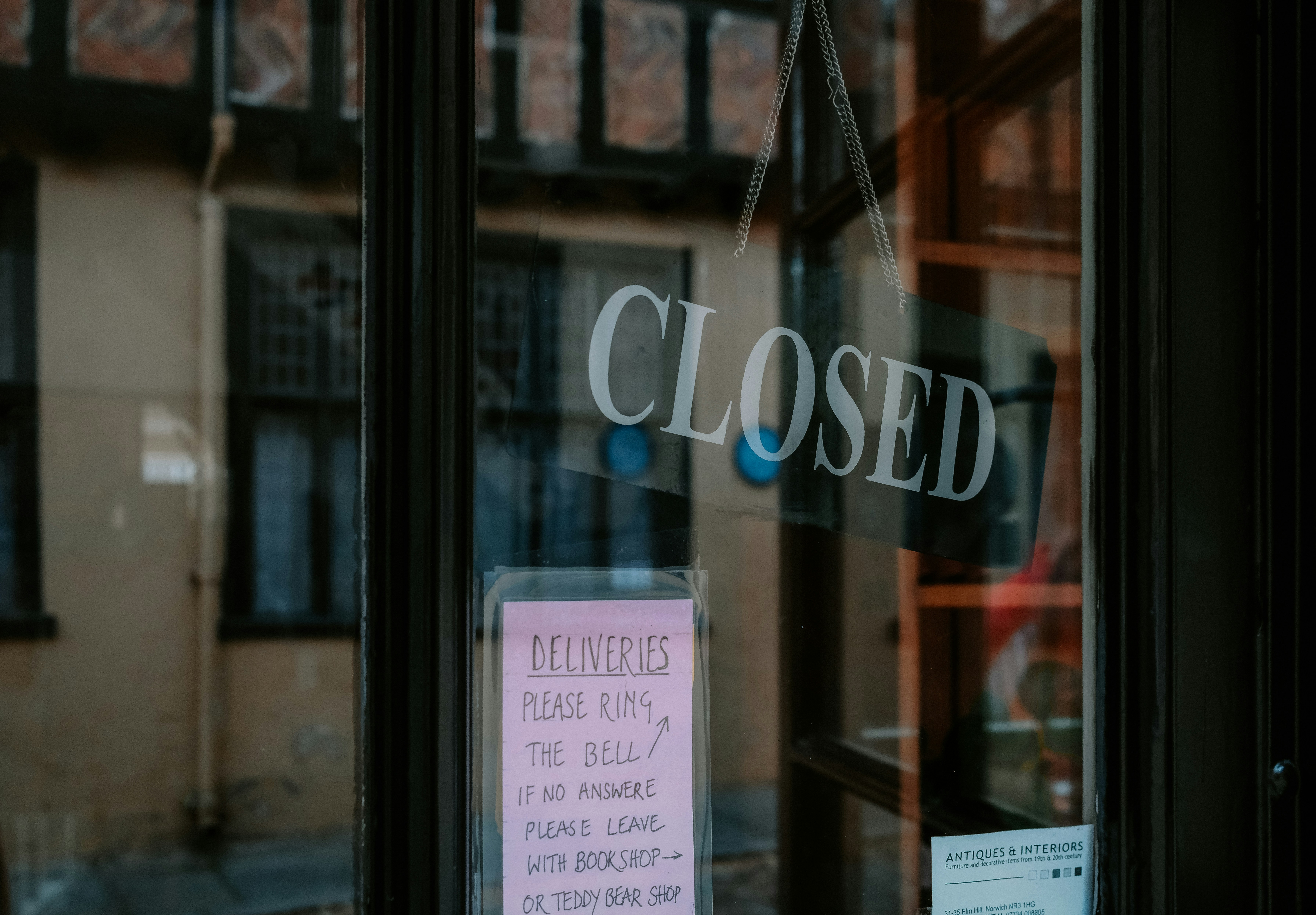 A Closed sign hanging inside a shop's glass door, above a handwritten pink note asking delivery drivers to ring the bell