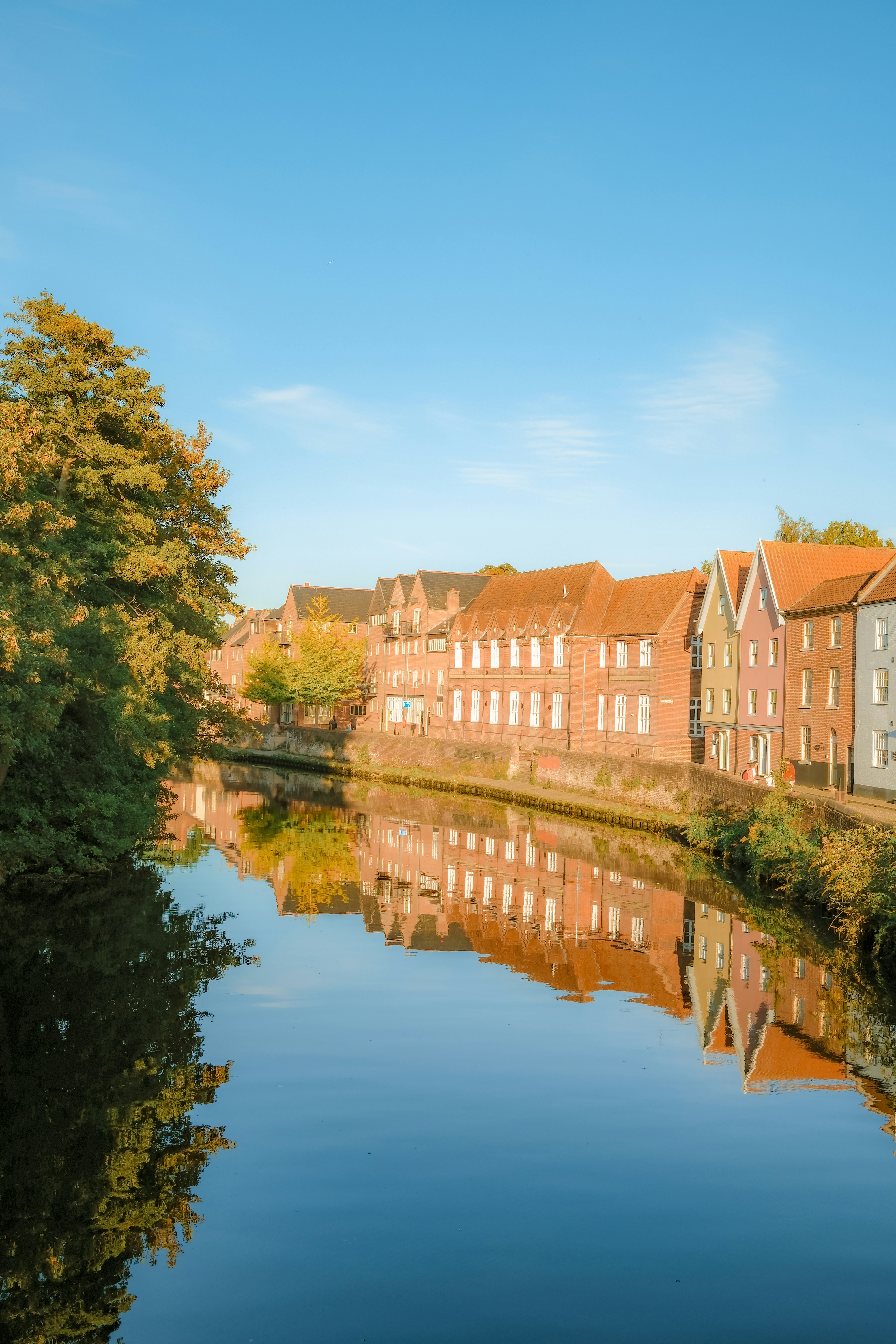 Colorful brick buildings reflected in a calm river under a clear blue sky