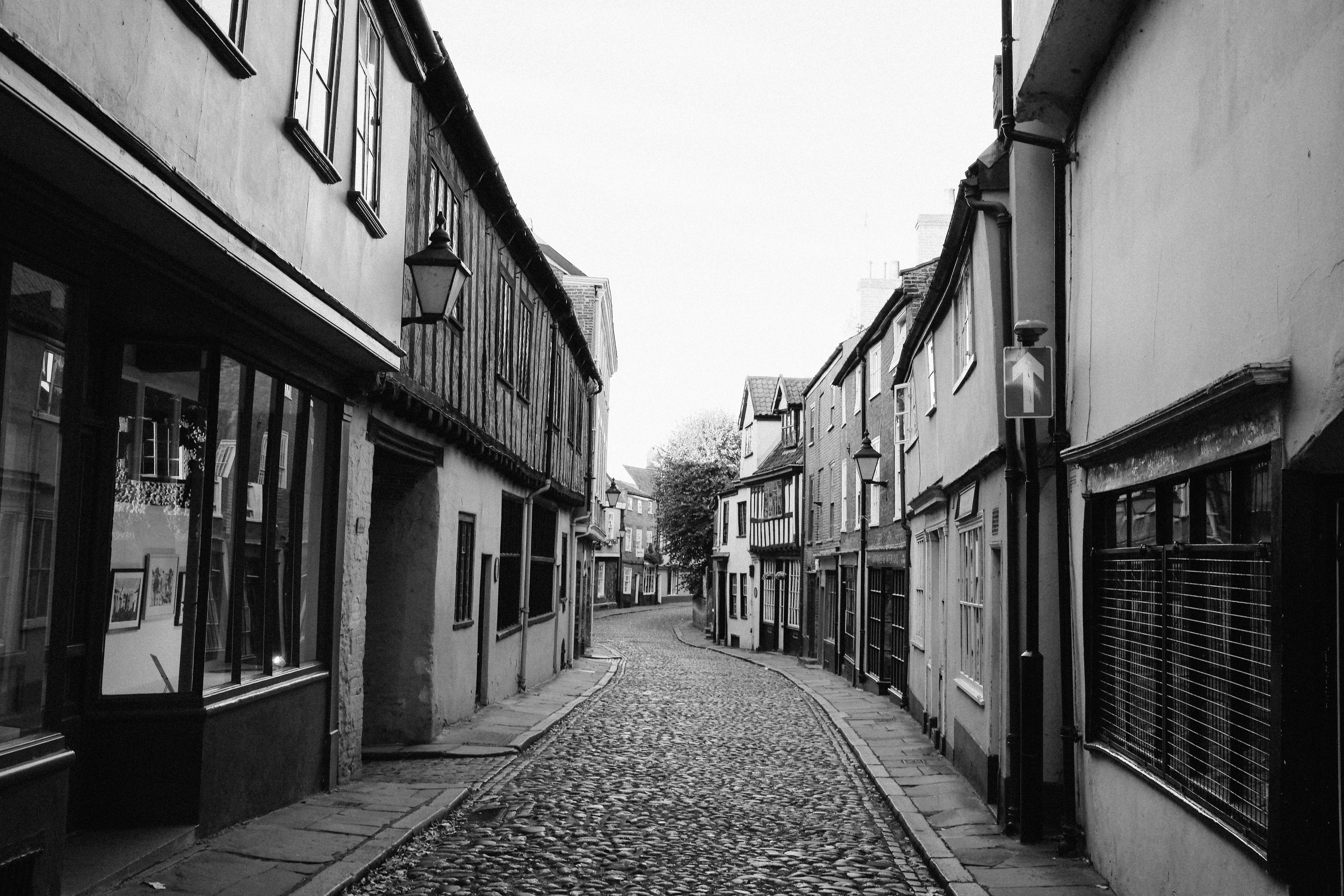 A narrow cobblestone street lined with historic timber-framed buildings in black and white