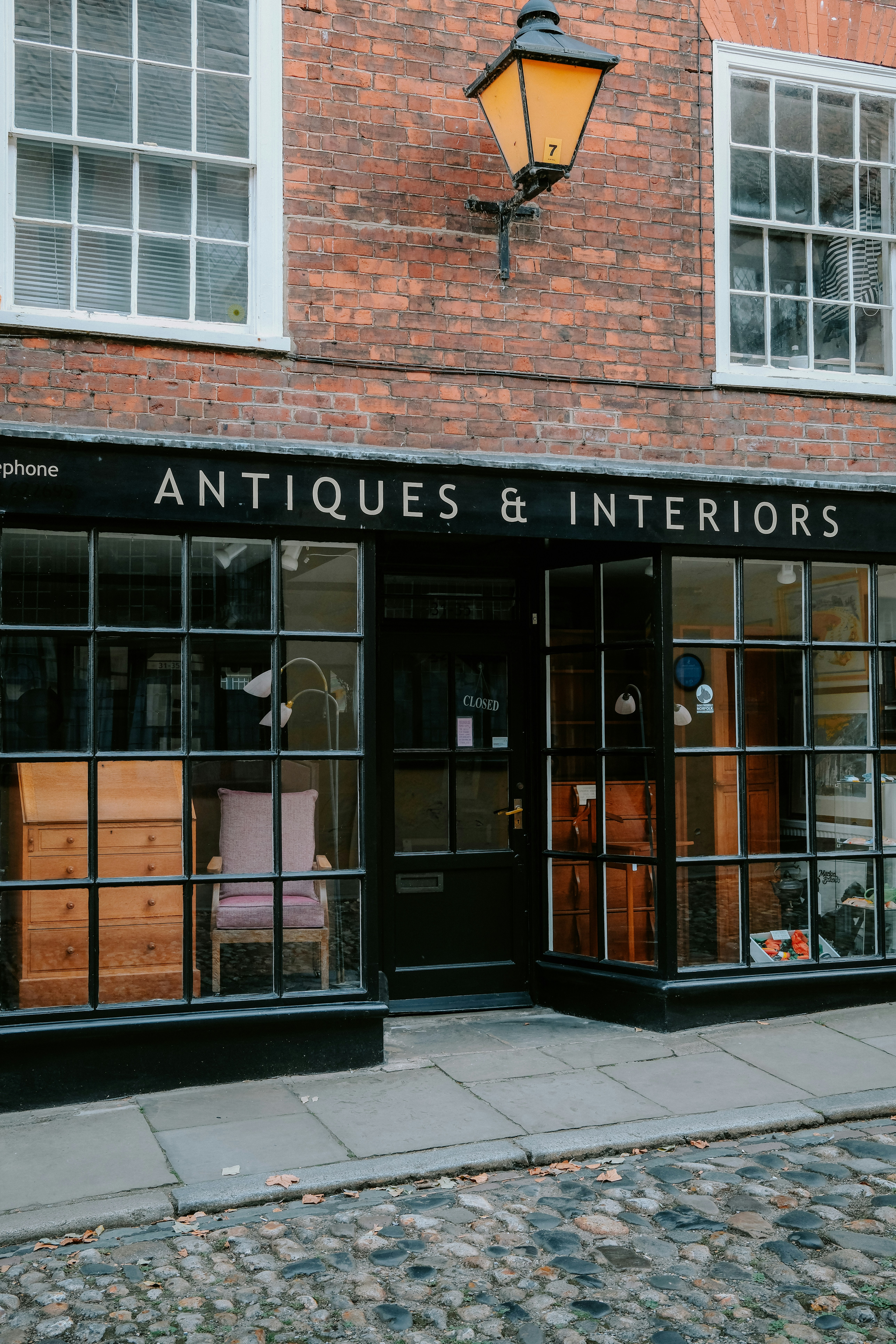 An antiques and interiors shop with a black storefront on a cobblestone street